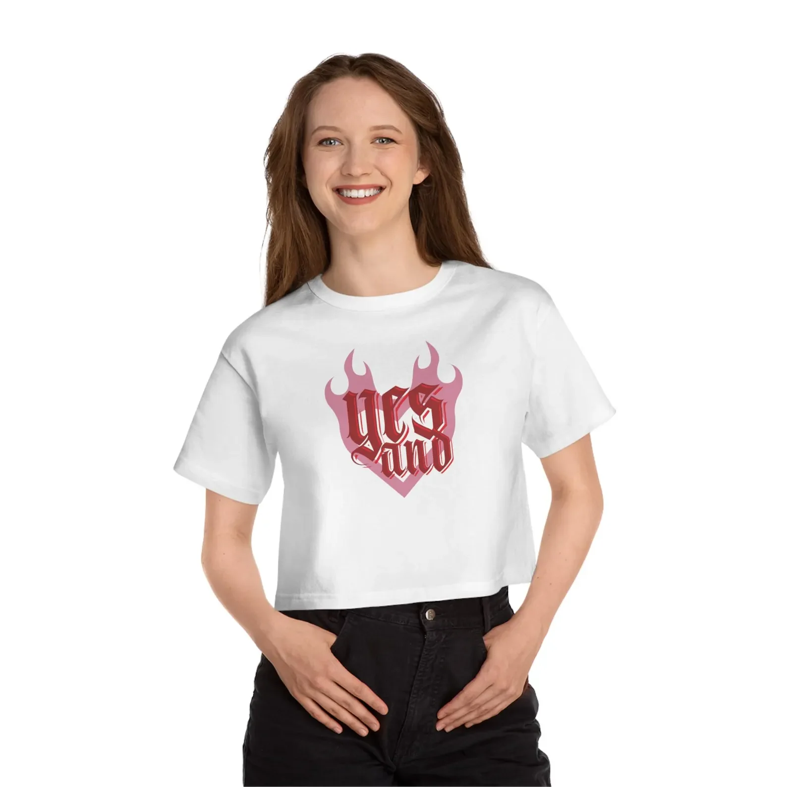 A woman wearing a white T-shirt with a red and pink flame design and gothic-style text reading "UC and". She has long, wavy red hair and is smiling while standing with her hands in her pockets against a plain white background.