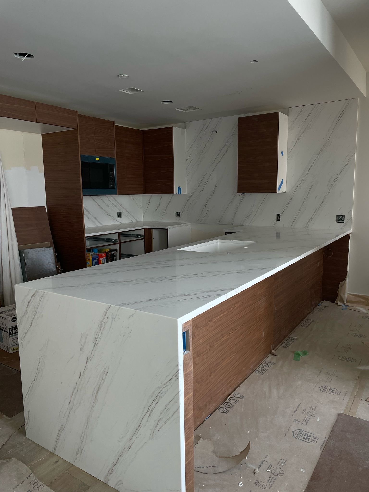 Kitchen under construction with white marble countertops, wooden cabinet framing, and unfinished floor.