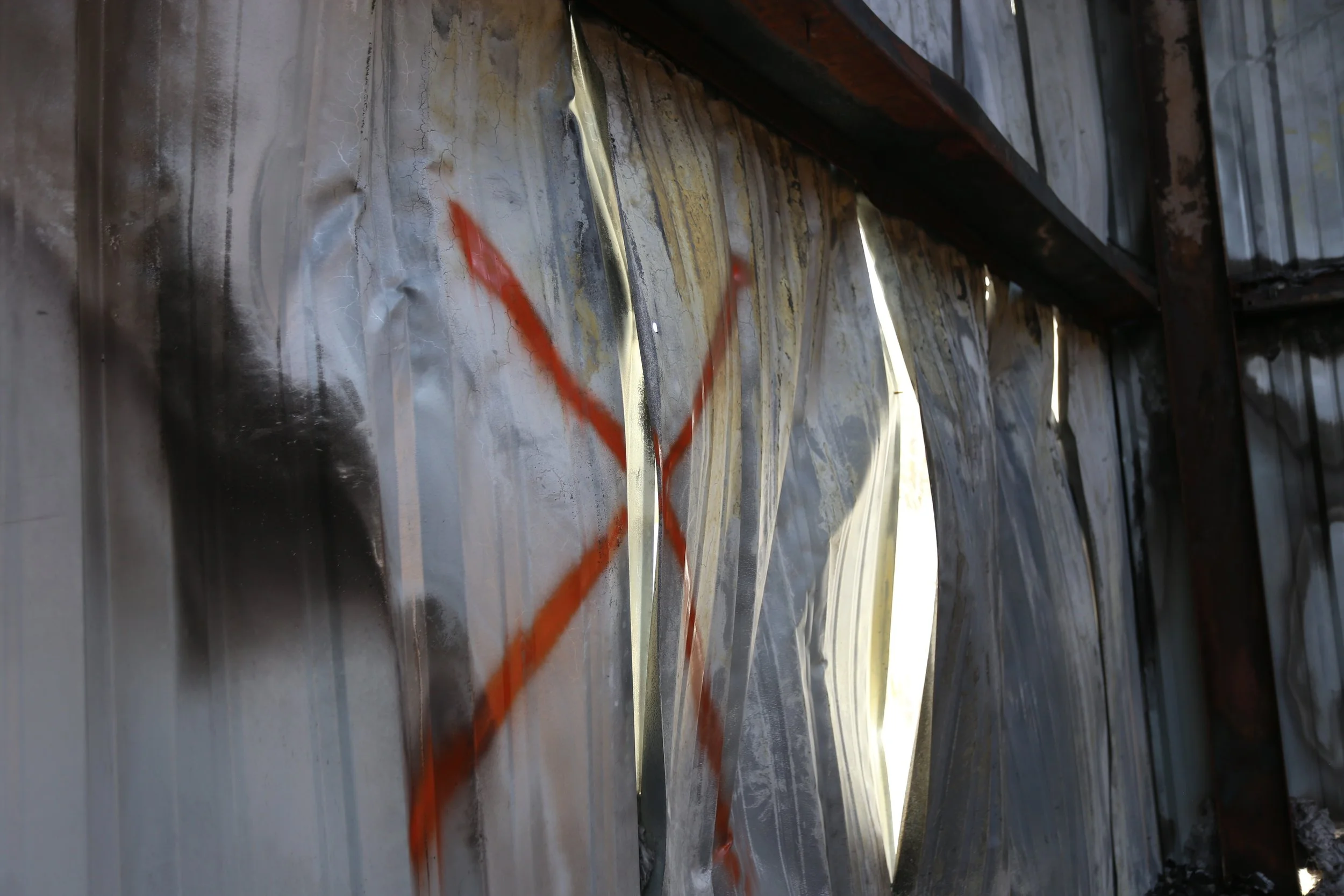 Close-up of a corrugated metal wall with some rust, paint splatters, and a wooden beam above.