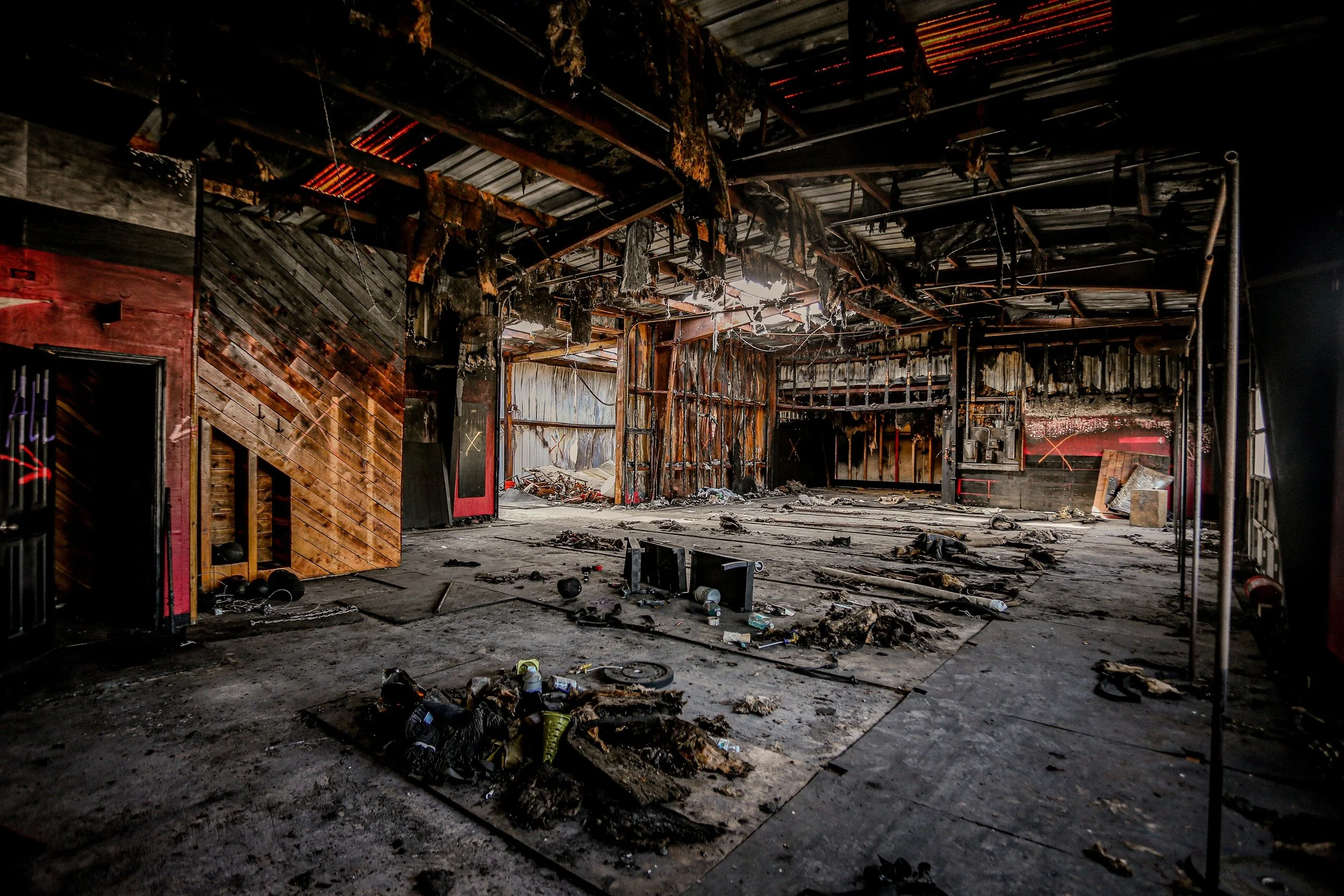 Interior of a building severely damaged by fire, with charred walls, burnt ceiling, and debris scattered on the floor.
