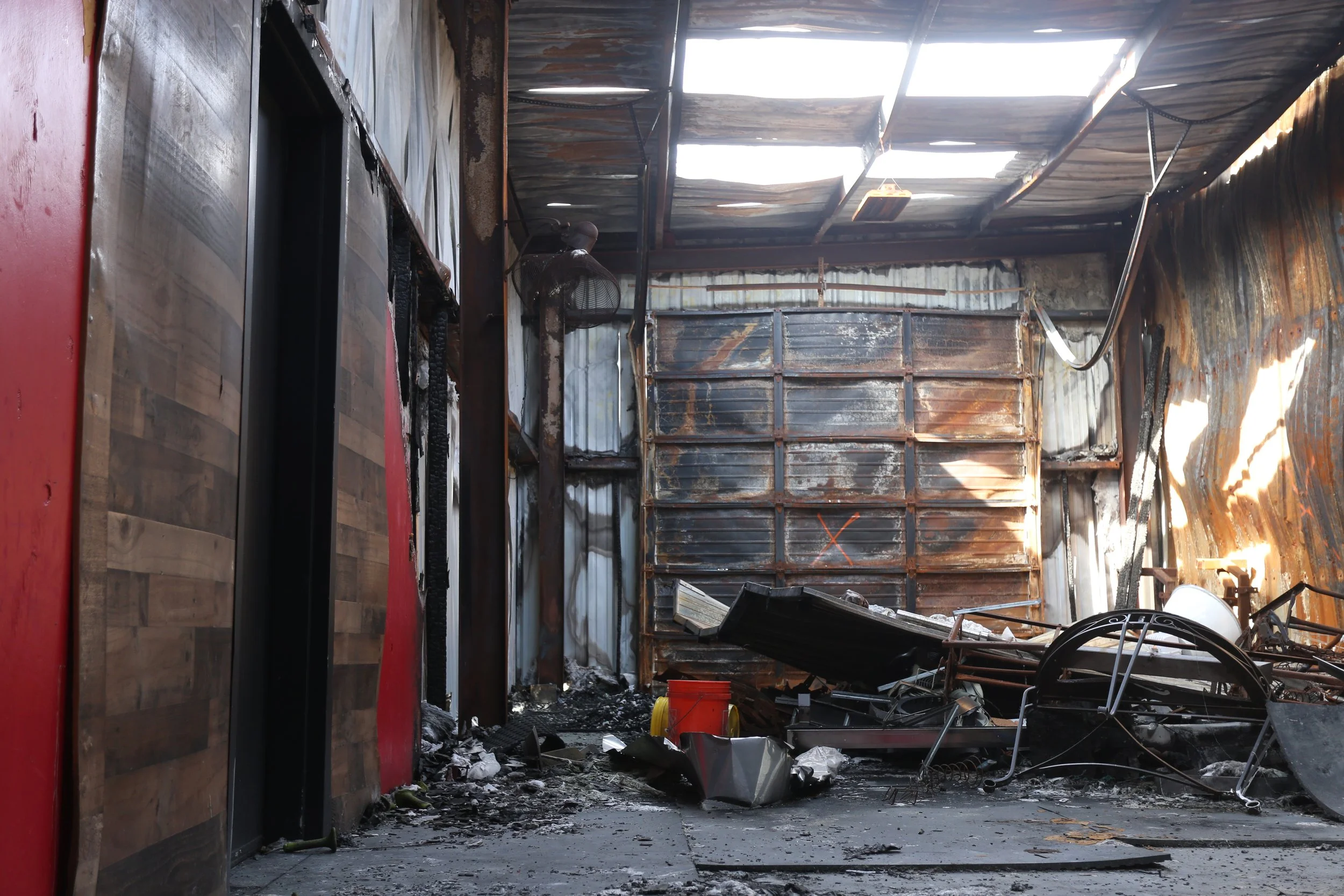 Interior of a building with fire damage, charred walls and debris on the floor, with a damaged ceiling and metal siding.