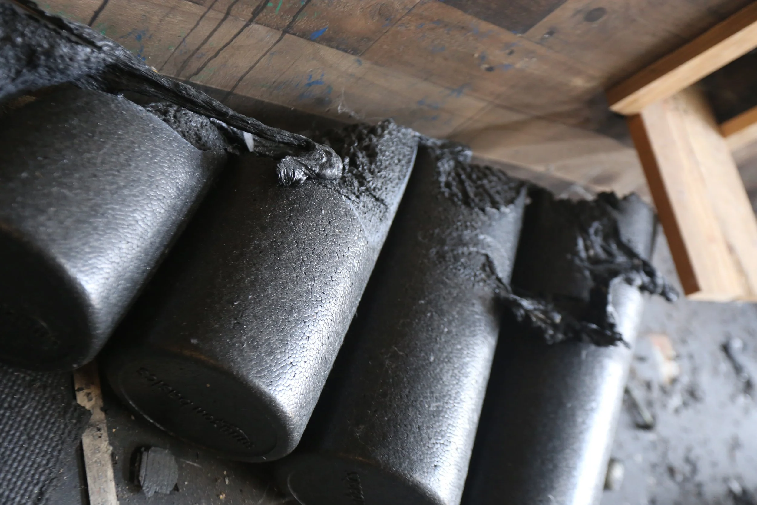 Close-up of black metal pipes with welding marks, set on a rough wooden surface and supported by a wooden frame.