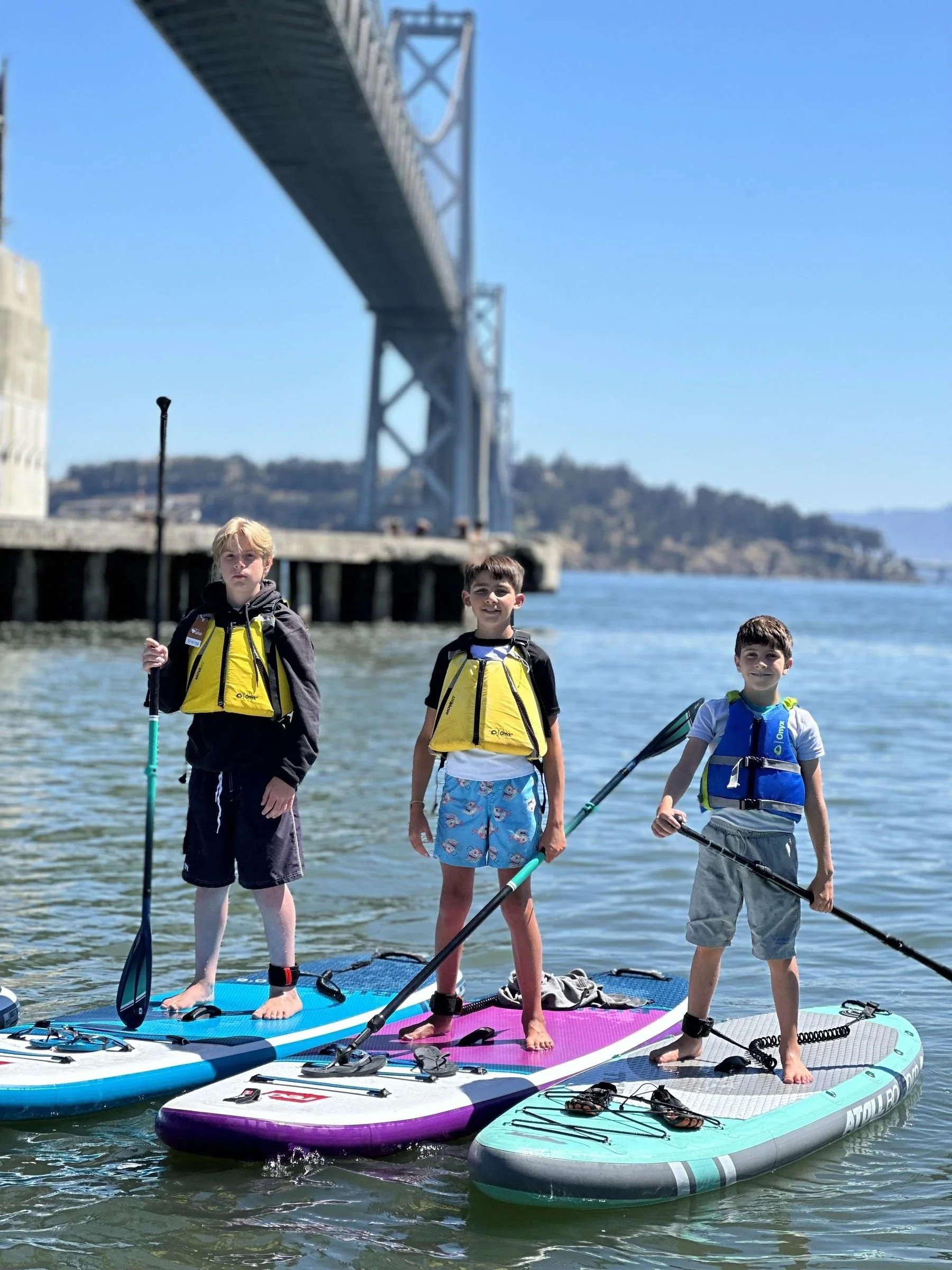 Campers paddleboarding near the Bay Bridge at advanced SUP camp