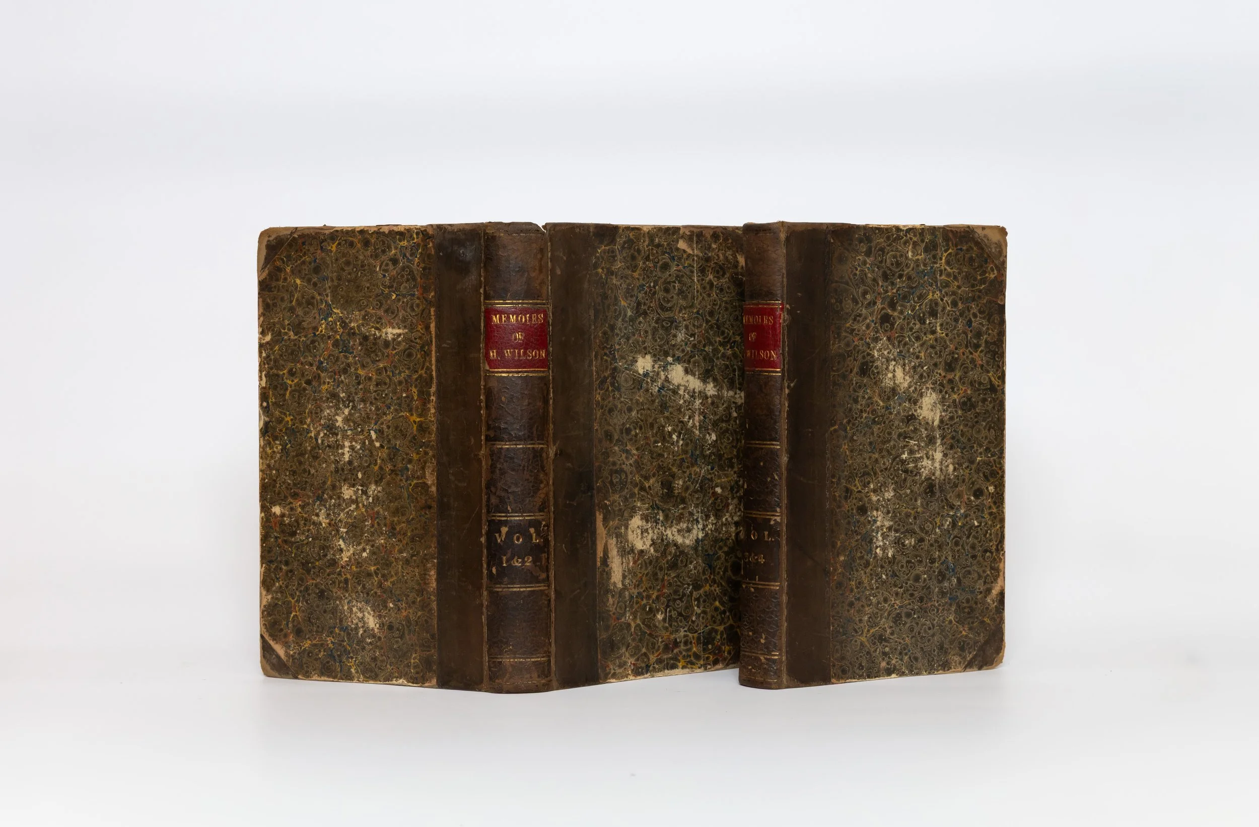 Two 18th century half calf over marbled boards on a pale background. Both have red spine labels. One is butterflied open.