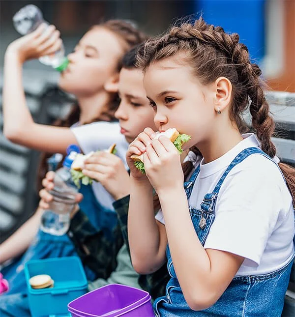three children eating lunch on a bench