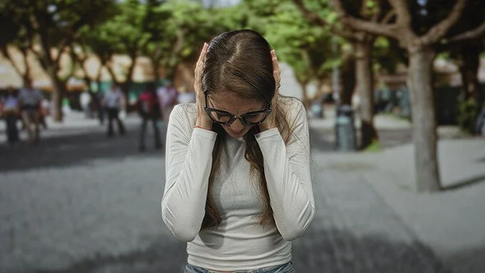 woman standing on quiet city street, covering ears
