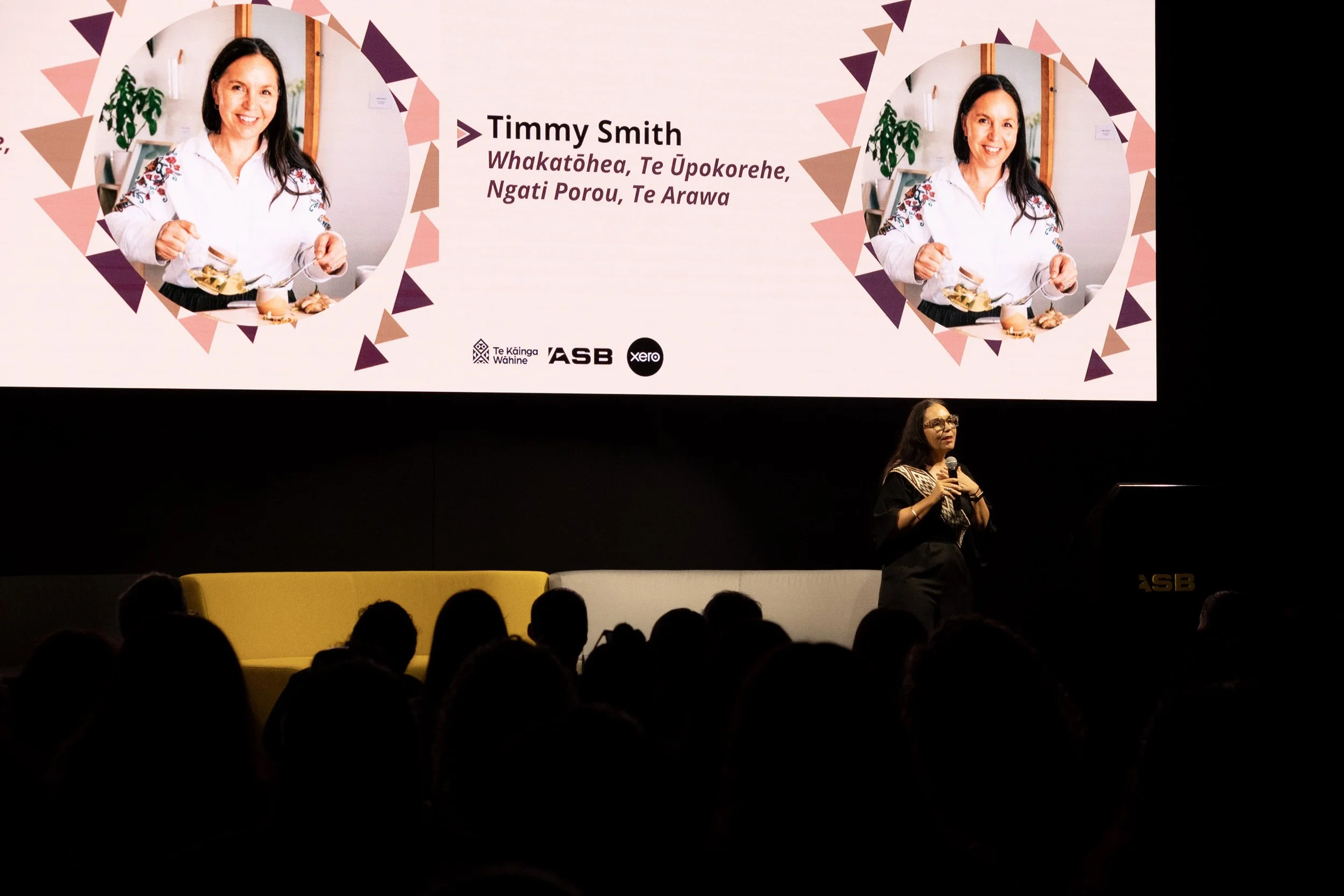 Timmy Smith on stage at Te Mana o Ngā Wāhine with a screen and her name behind her