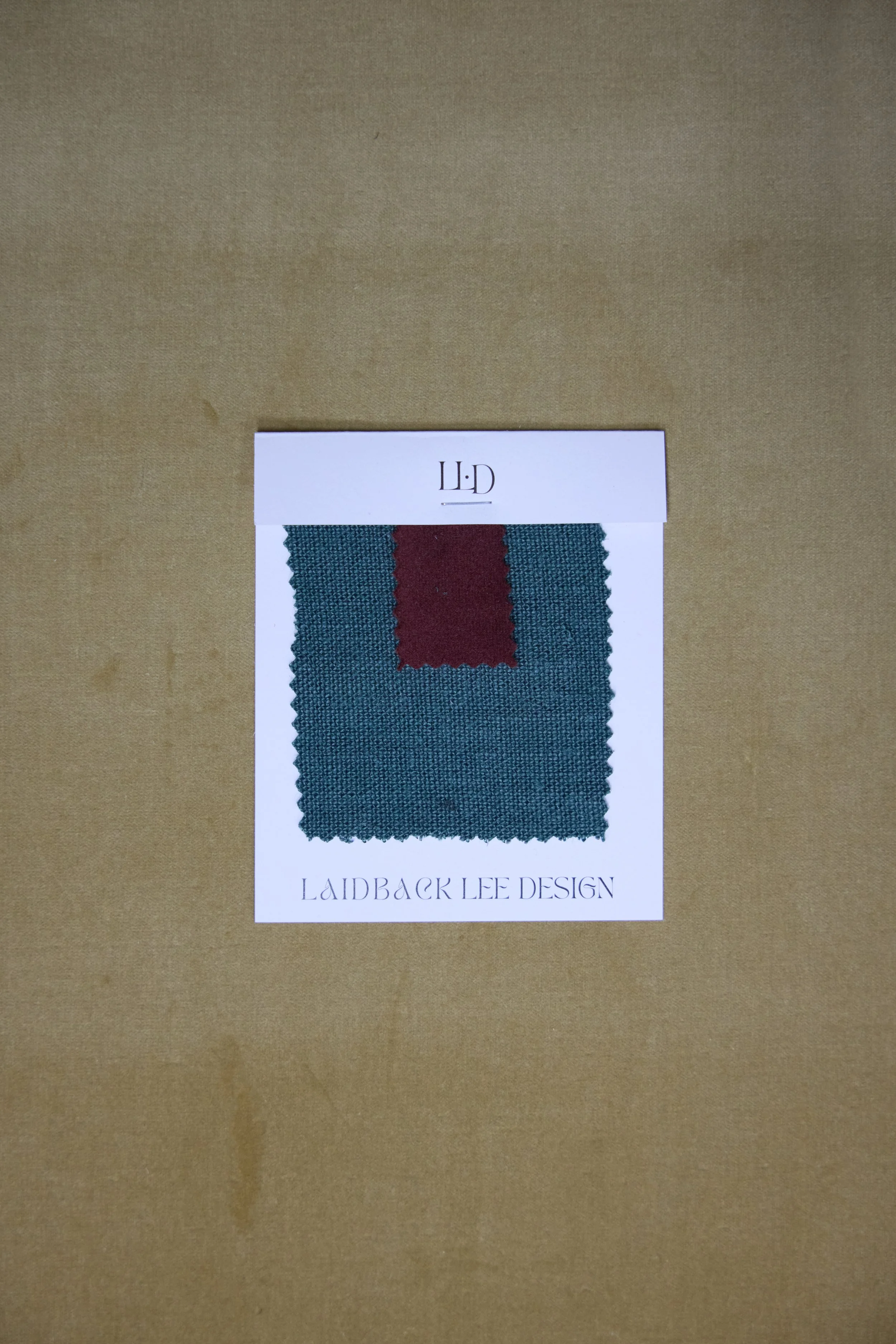 Fabric swatch sample with teal and red colors, labeled 'Laidback Lee Design' and contained on a white card.
