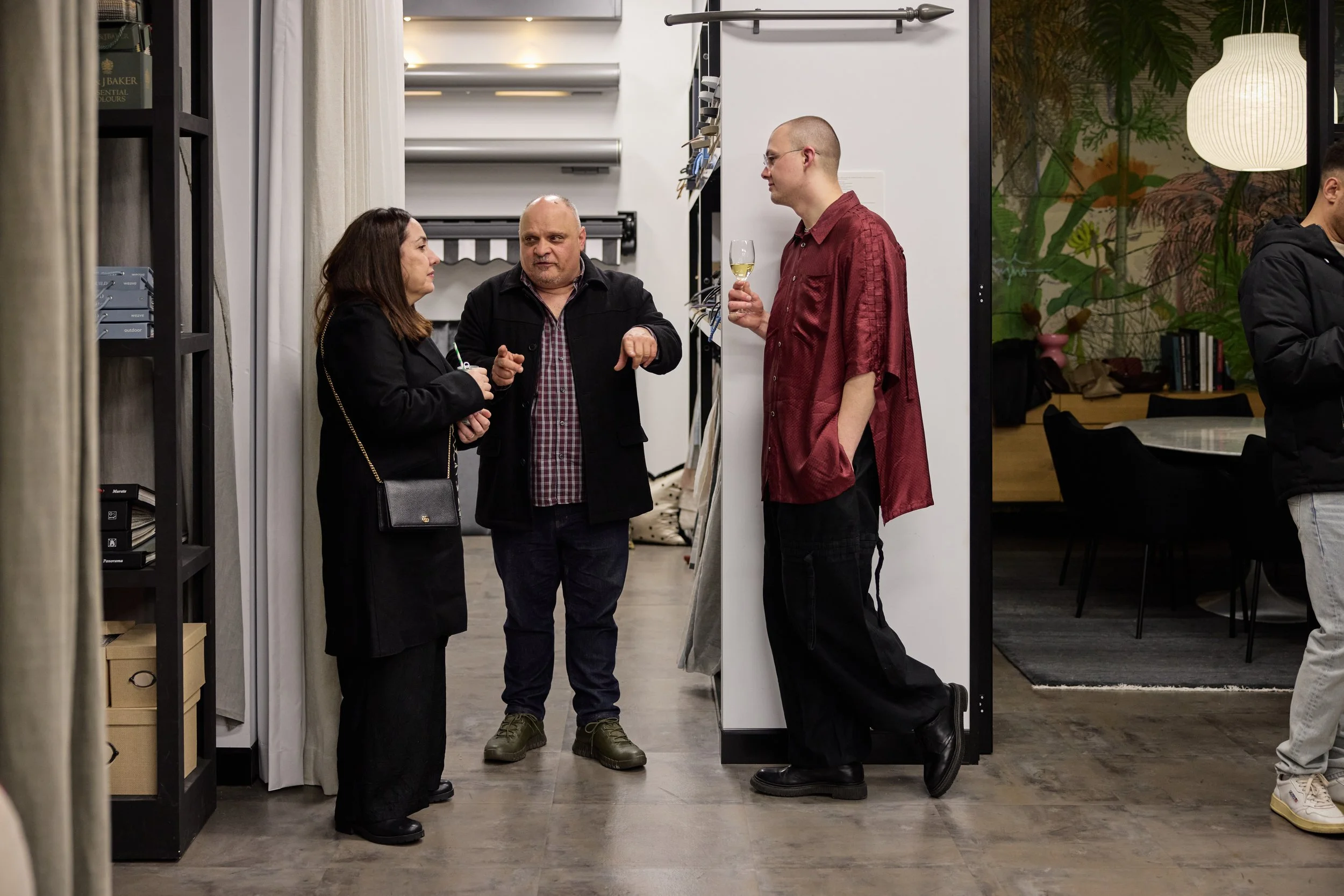 Group of four people engaged in conversation in an indoor setting, with one holding a glass of white wine.