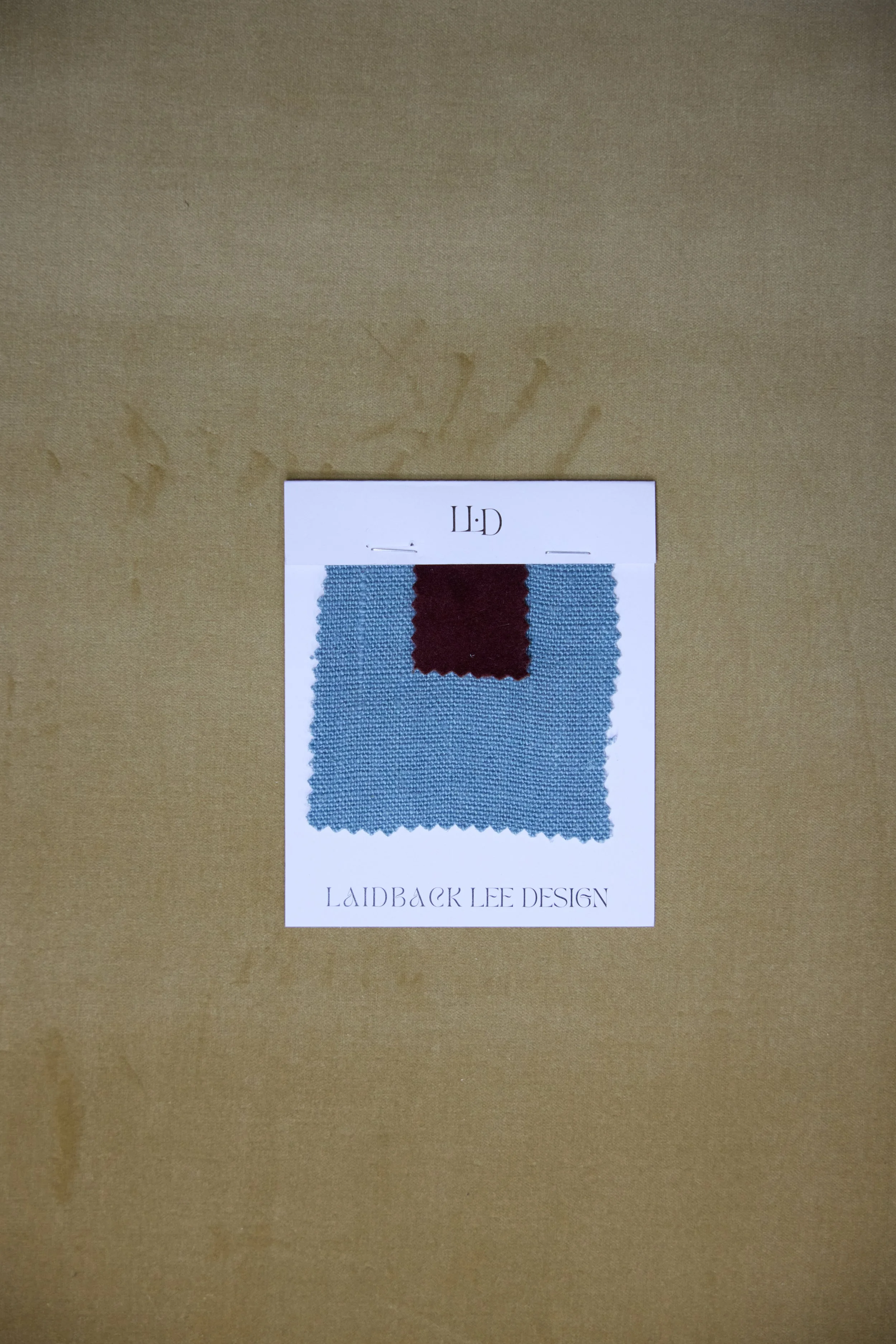 Swatch of fabric with blue and burgundy colors on a white card labeled 'LAIDBACK LEE DESIGN'.