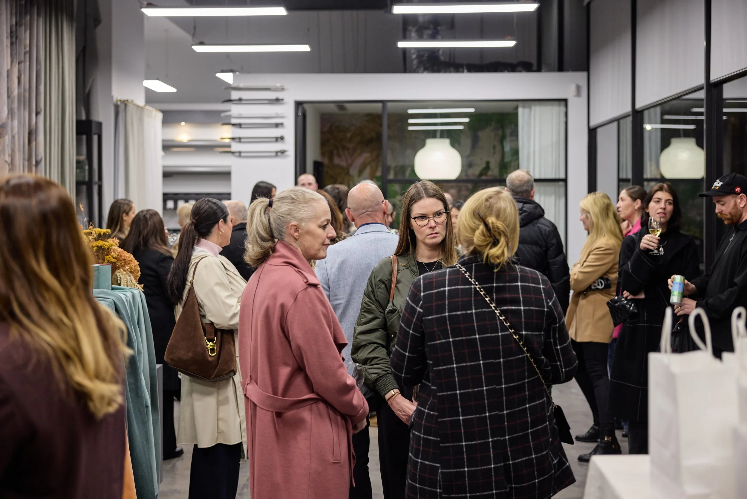 People attending a social gathering or event in an indoor space, engaging in conversations and holding drinks.