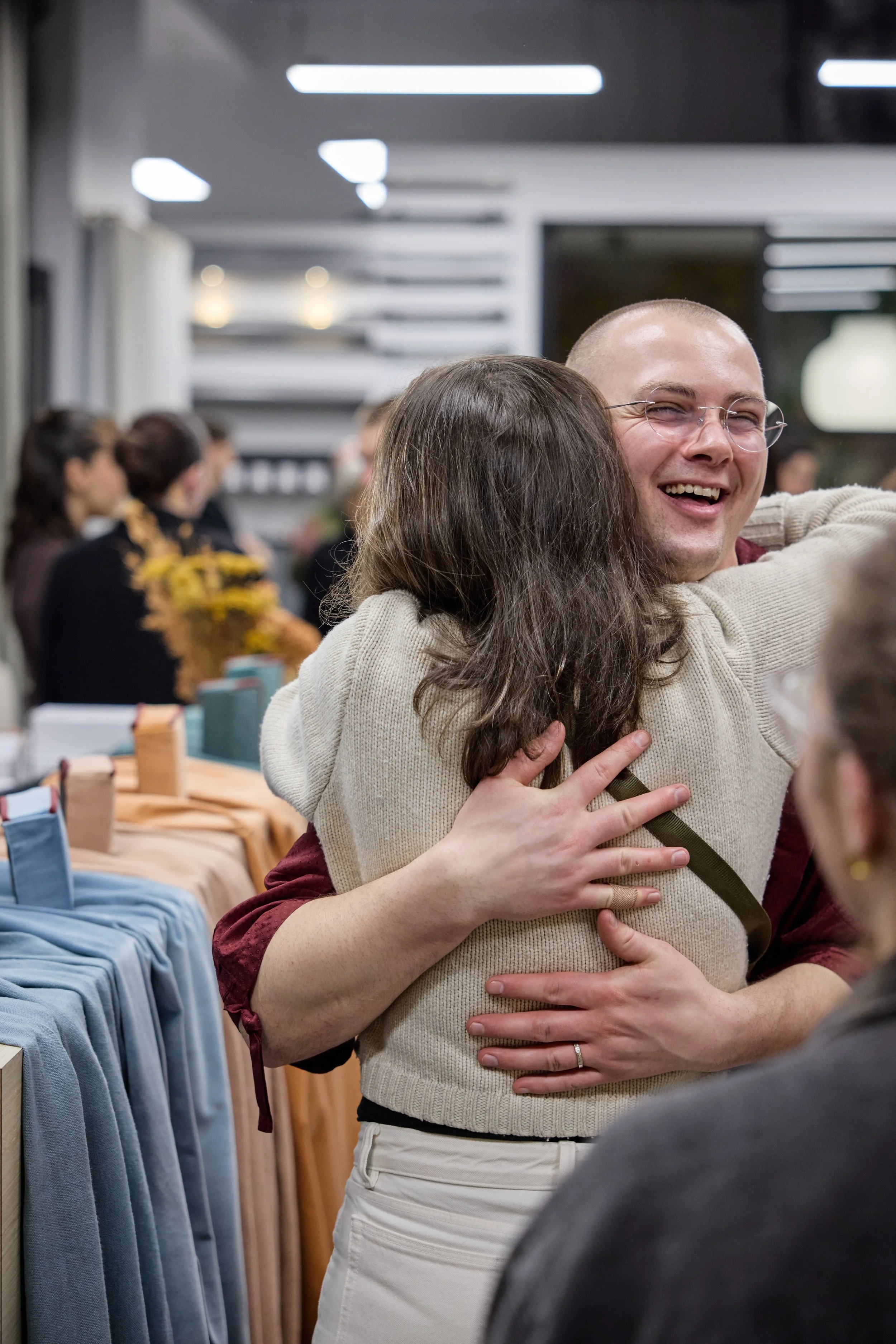 People hugging and smiling at a social gathering or event inside a modern venue.