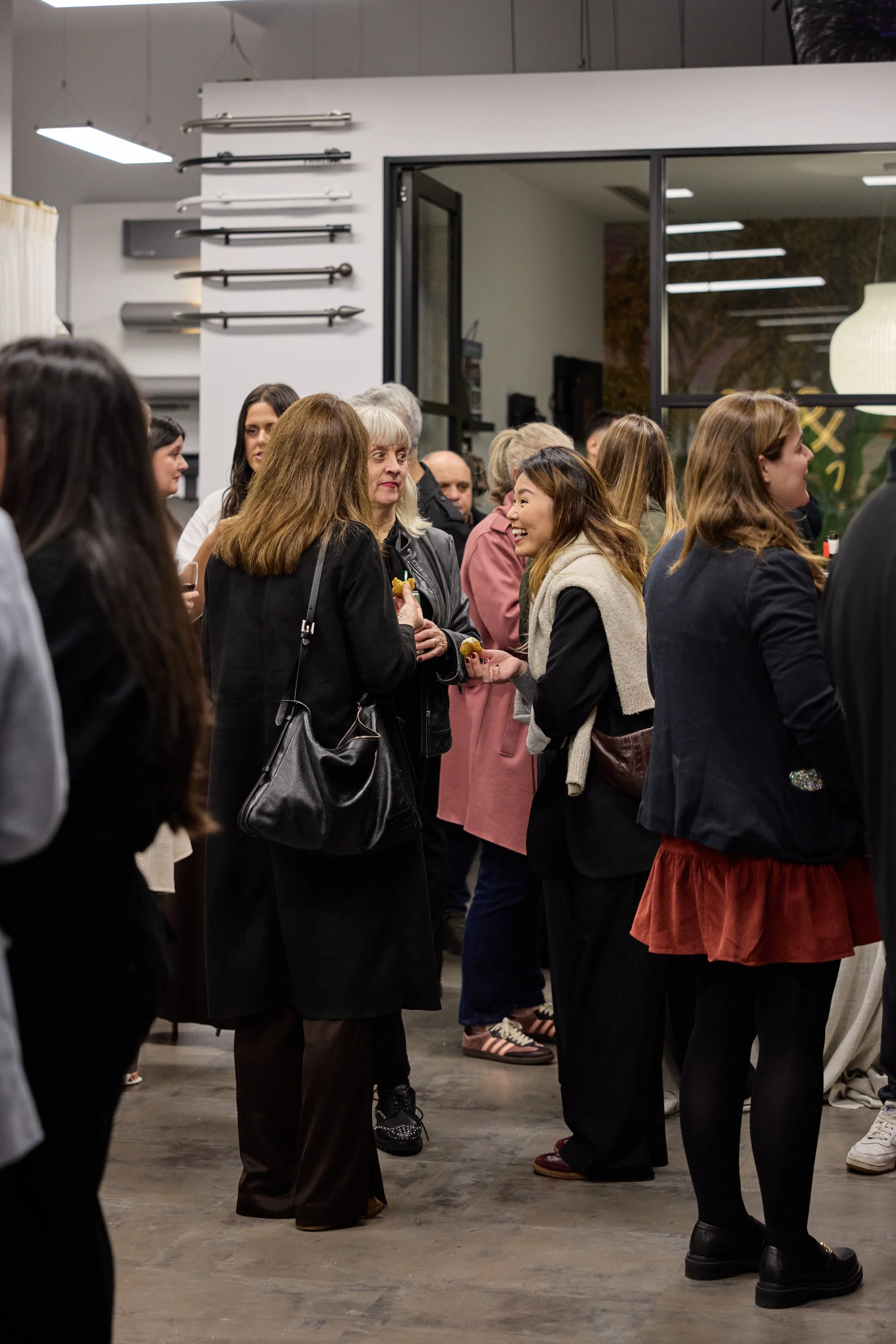 People at a social gathering or event indoors, conversing and smiling, with some holding food and drinks.