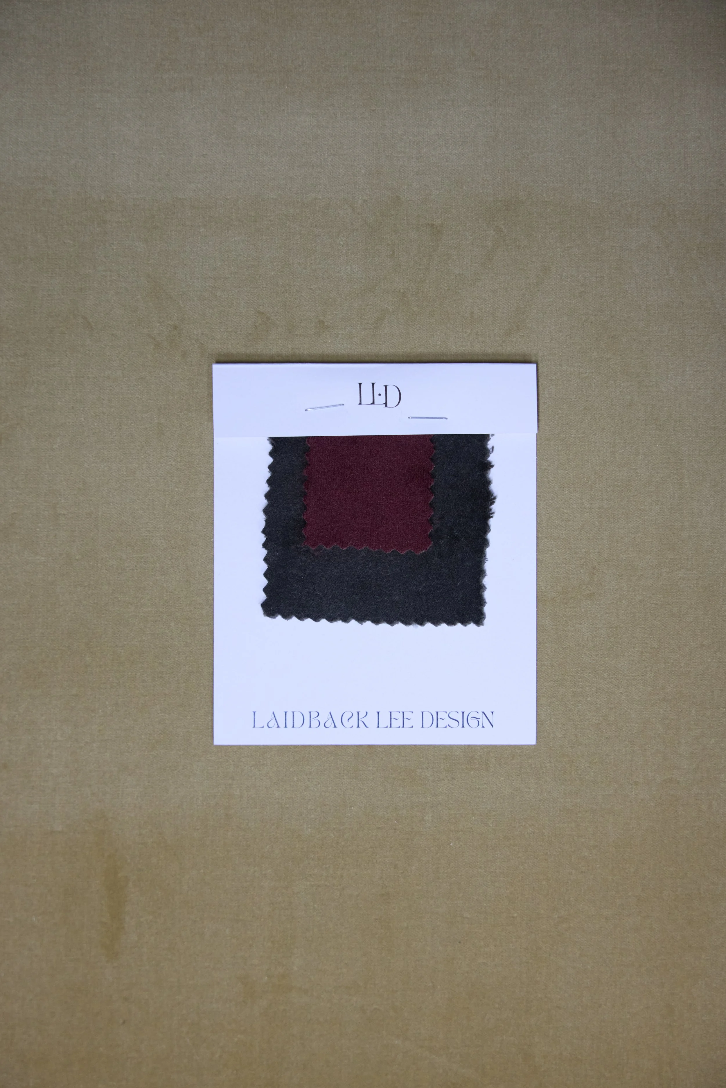Fabric swatch sample with burgundy center and black border on a white Laidback Lee Design card.