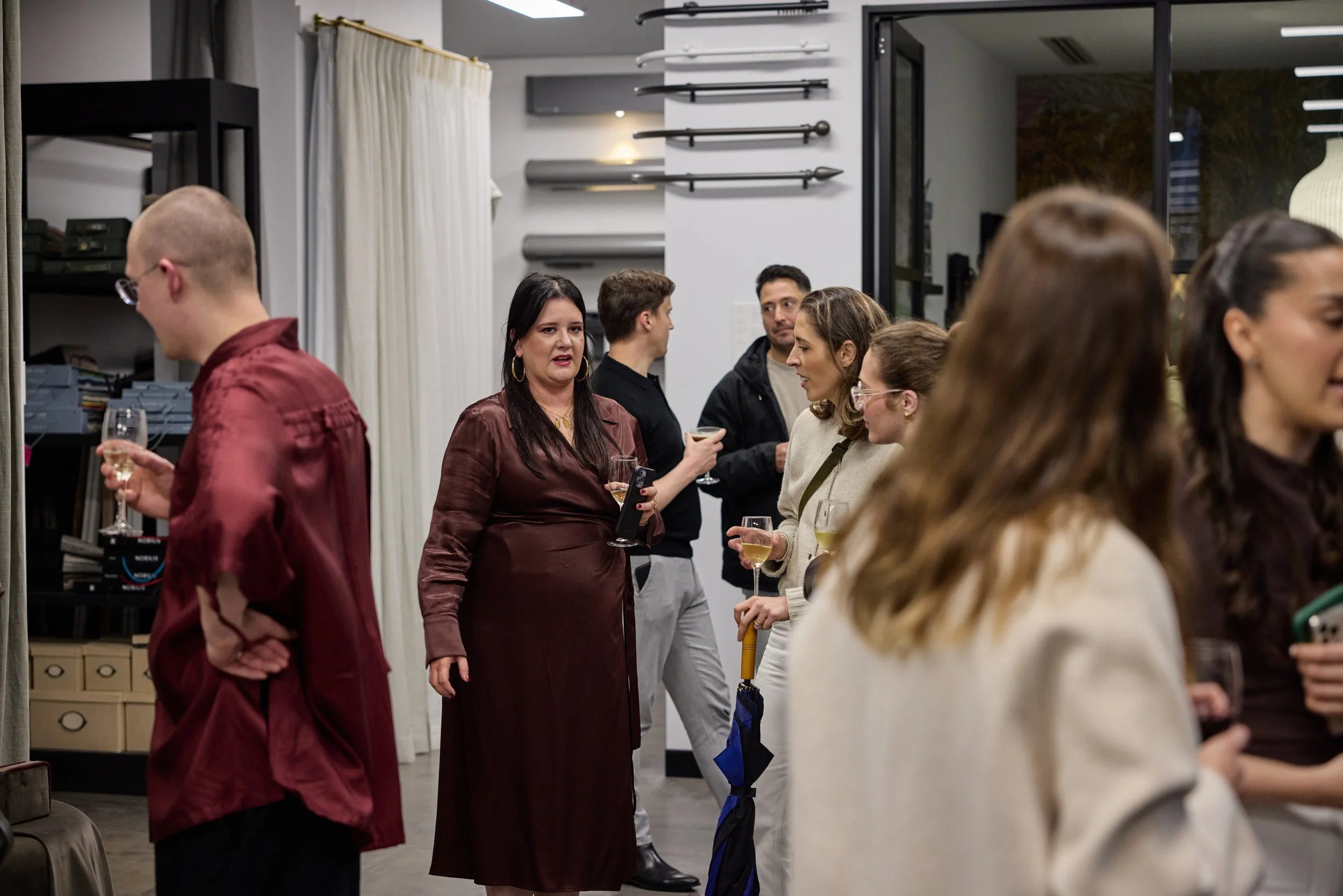 Group of people socializing at a gathering, holding wine glasses and engaging in conversation inside a modern room.