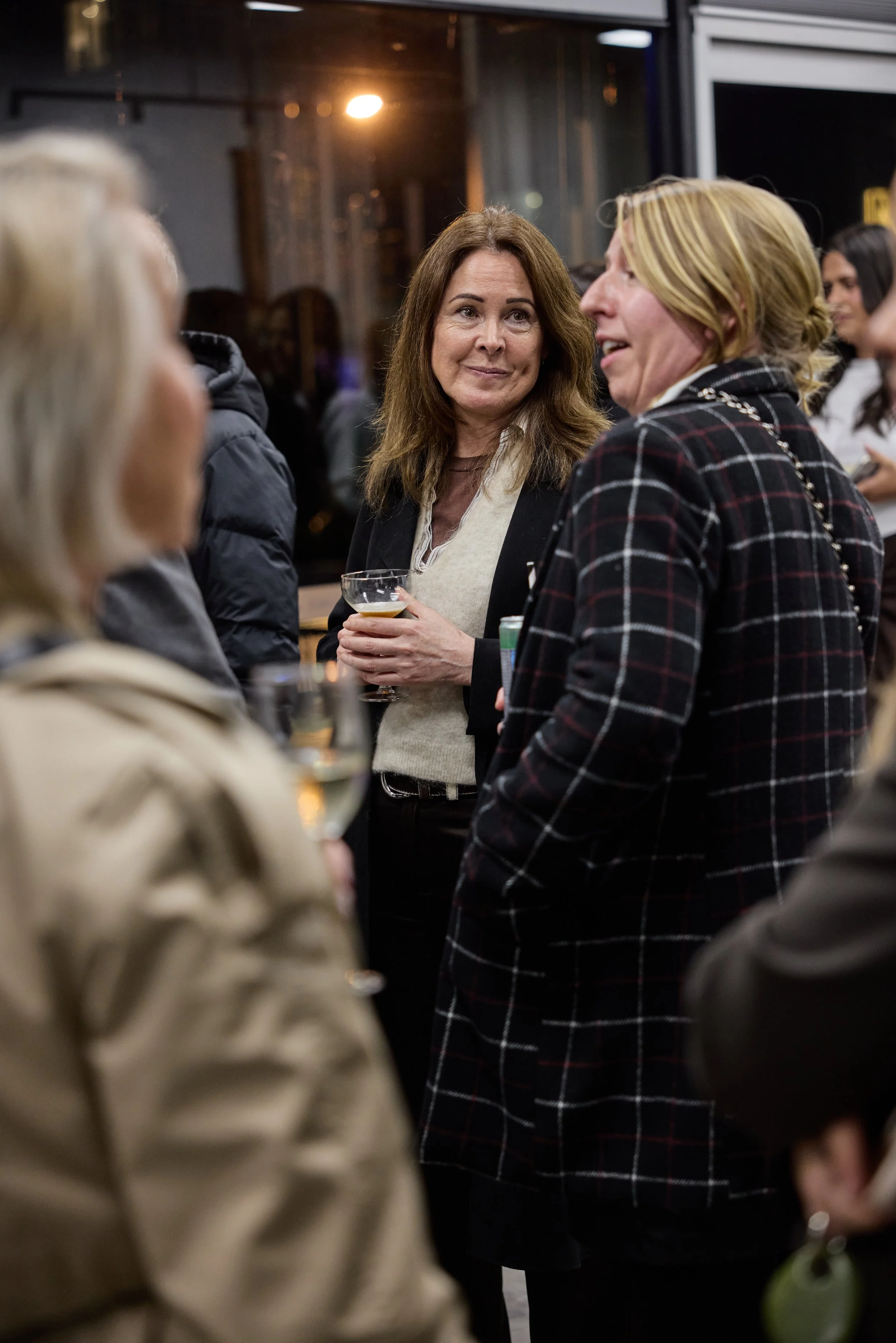 Group of women socializing at an indoor gathering, holding drinks and chatting.