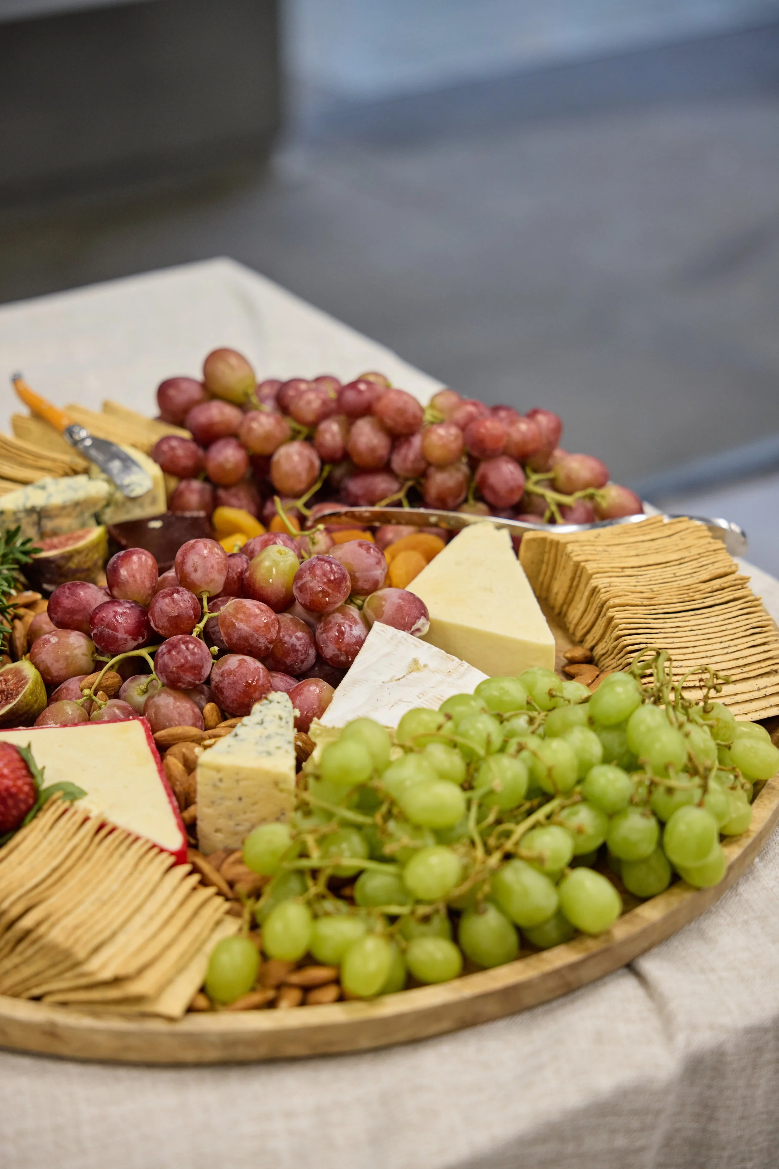 A cheese and fruit platter featuring grapes, assorted cheeses, crackers, and almonds on a wooden tray.