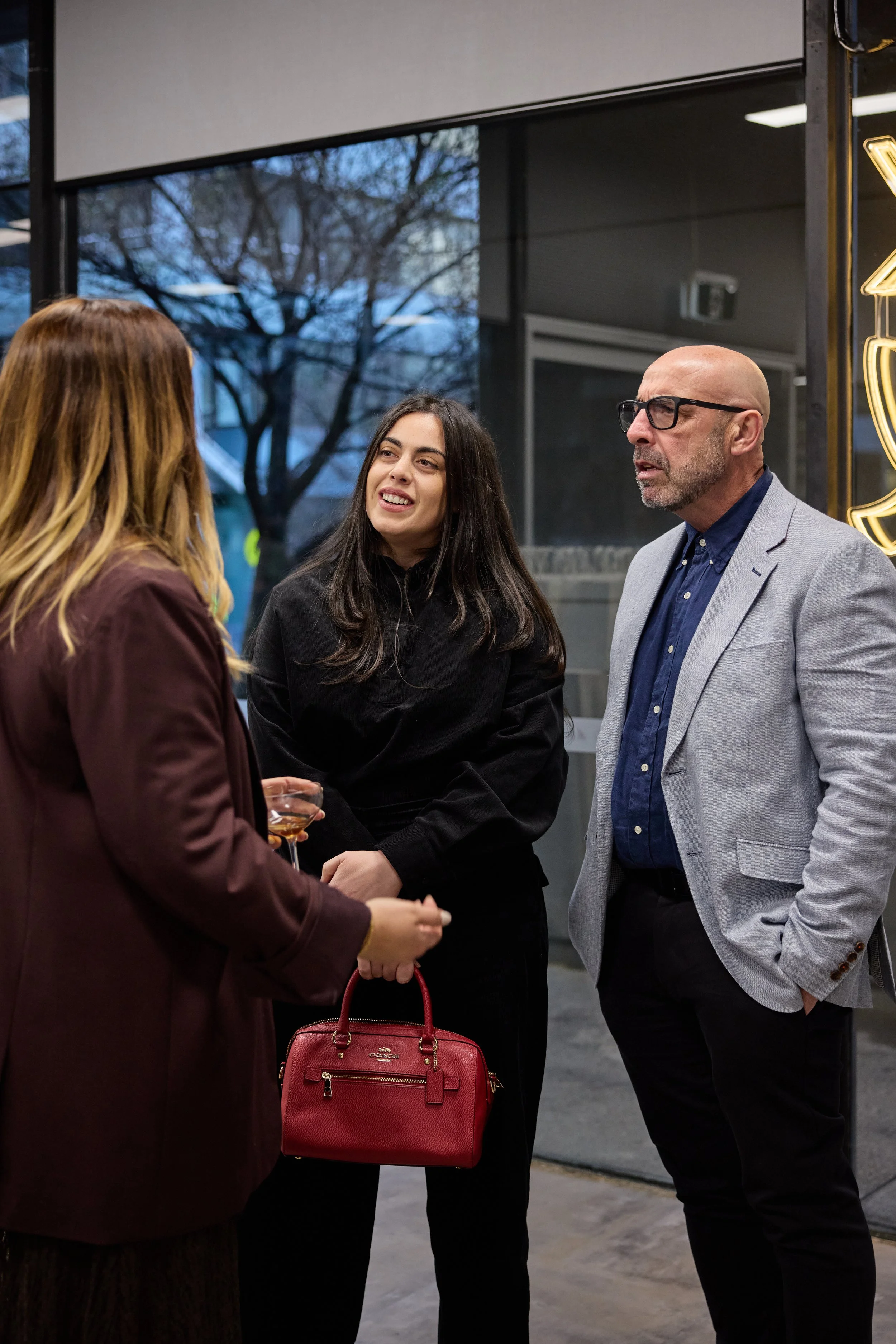 Three people in business attire having a conversation outside a building in the evening.