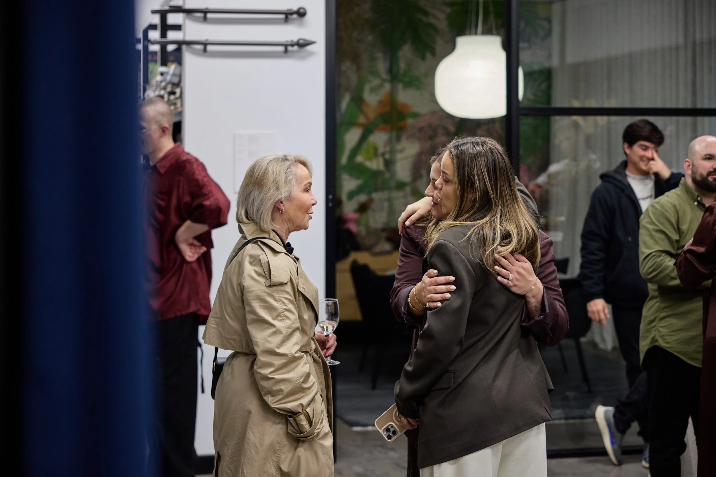 People talking and hugging at a social gathering in an indoor space with modern decor.