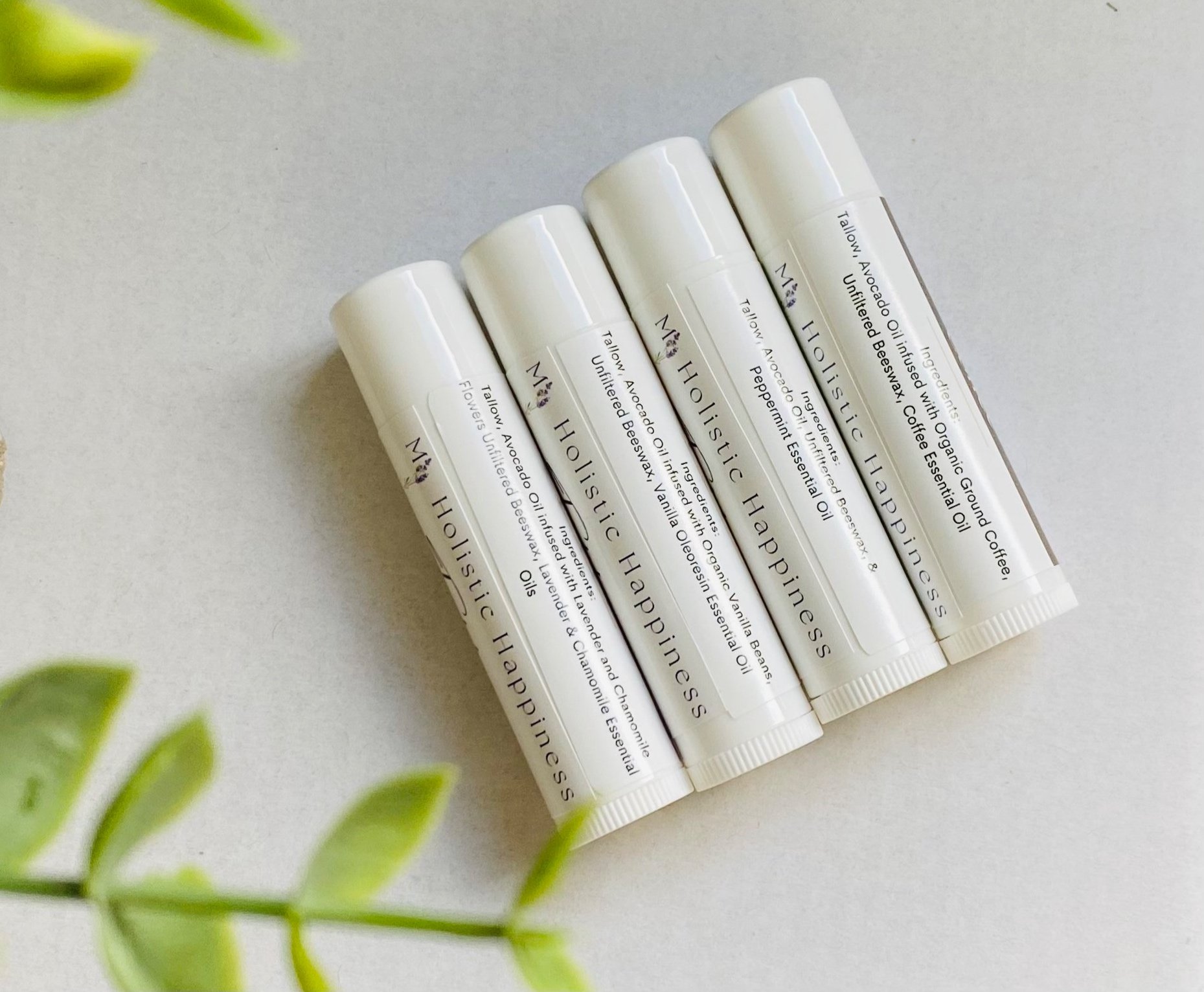 Four tubes of natural lip balm lay side by side on a white surface. Each label is showing the natural ingredients.