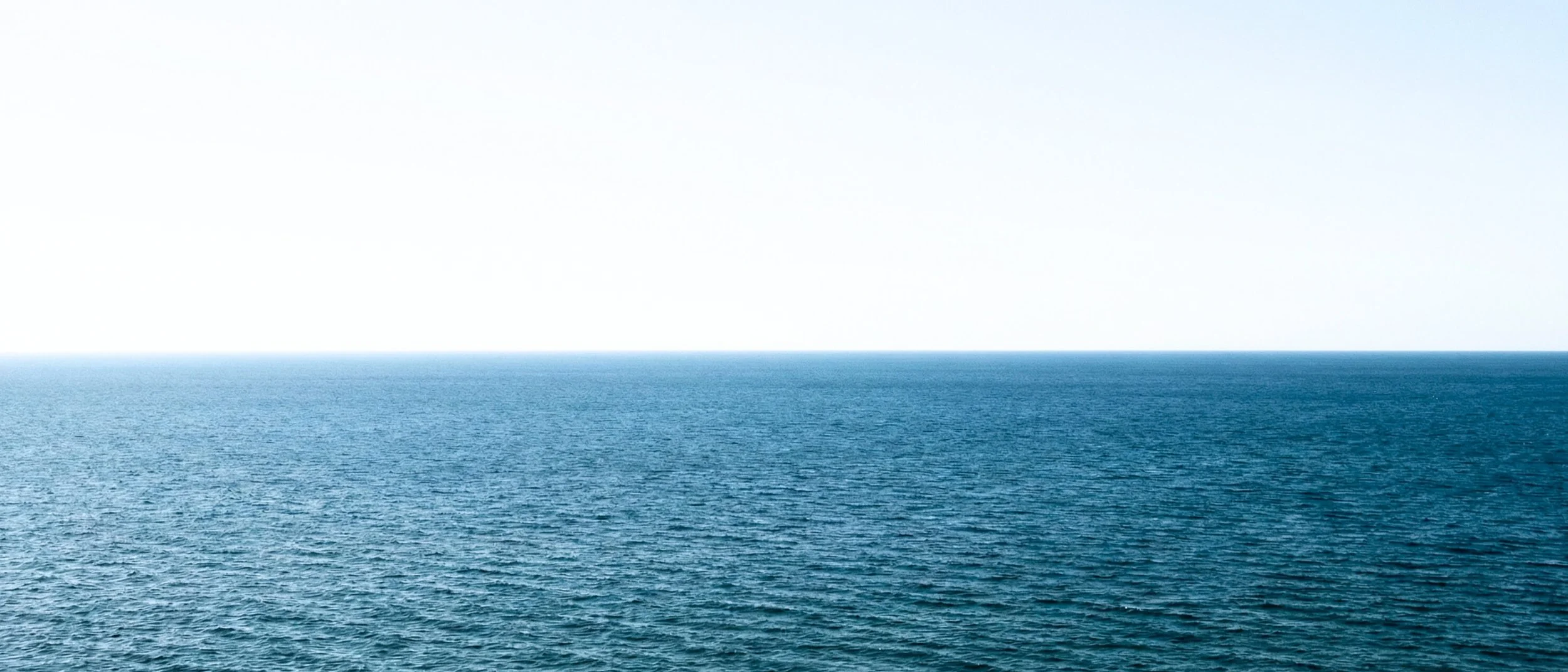 A vast ocean with gentle waves, under a clear, bright sky.