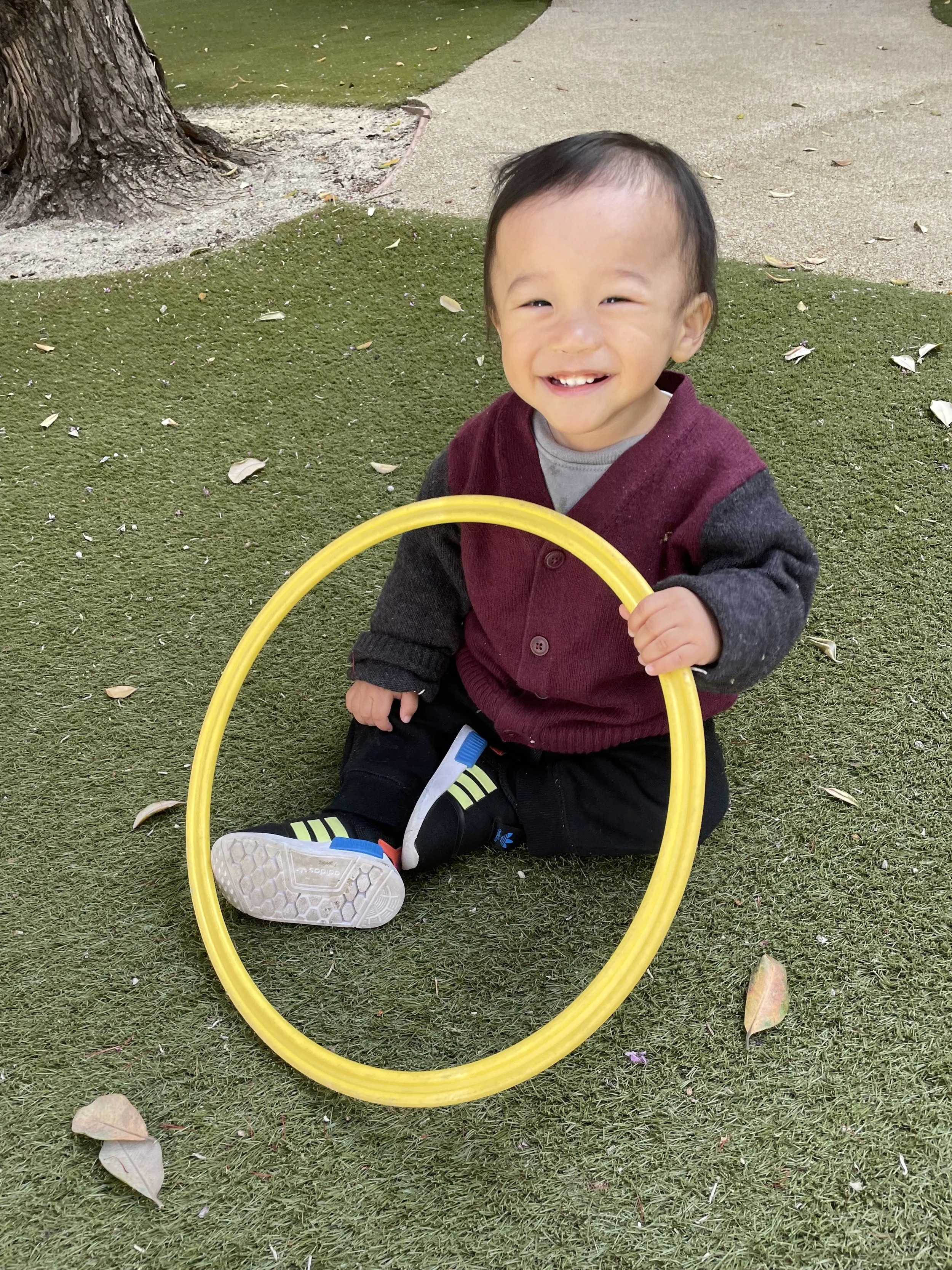 smiling toddler sitting on ground holding a yellow play ring