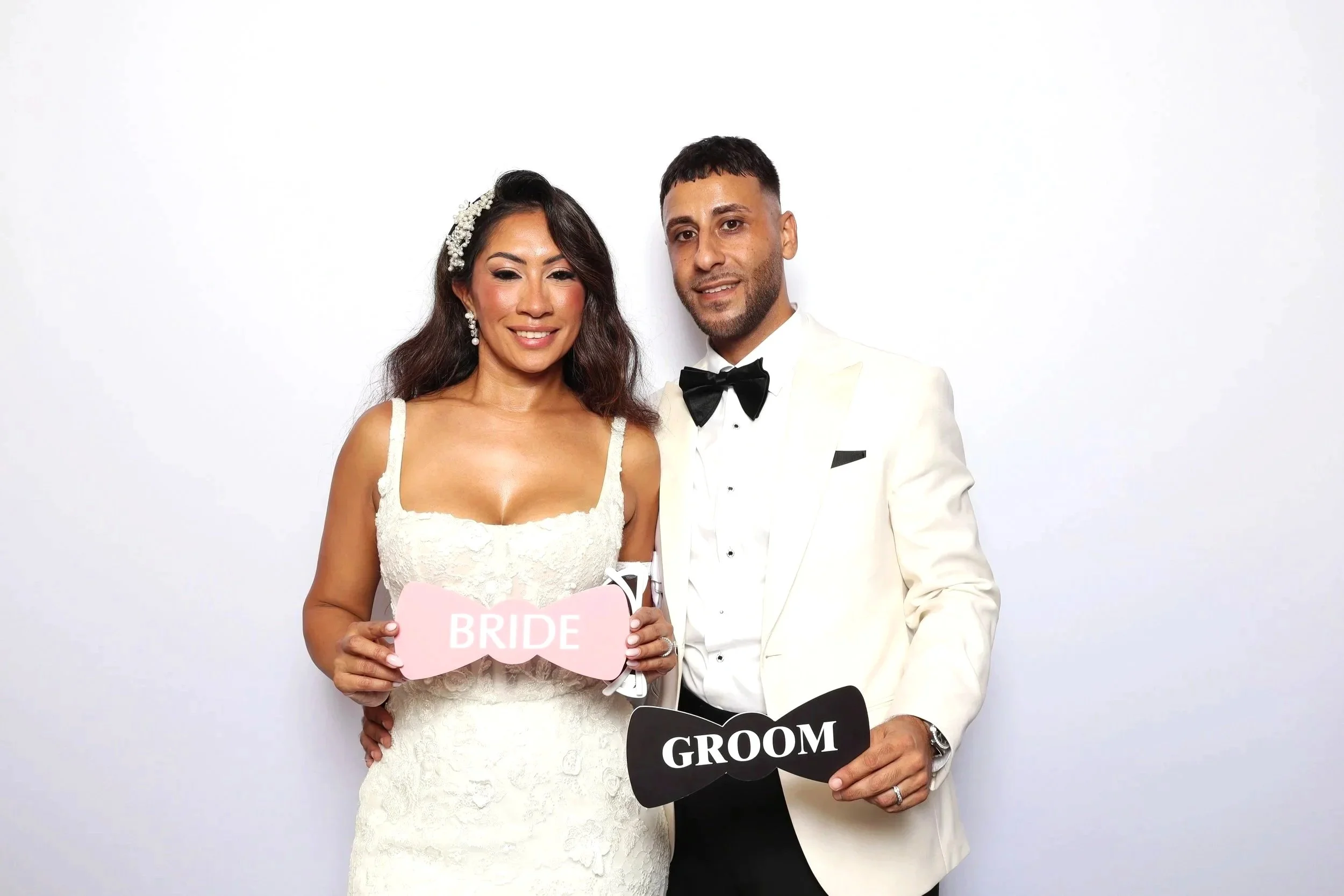 Bride and groom in white attire posing with a GROOM sign at photo booth rental in Key Biscayne, FL — D&amp;L Photobooths