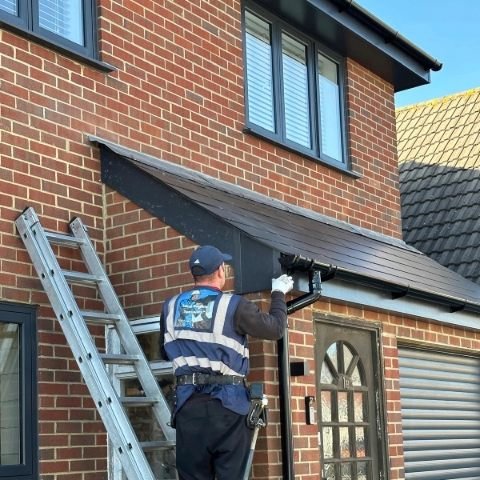 Image showing the front of a detached property in Poole where a fitter is installing new anthracite grey UPVC bargeboards and box ends