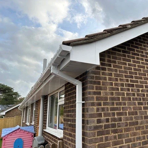 Close-up of the corner of a brick house showing new white fascias, soffits and bargeboards and a one piece box end in white upvc
