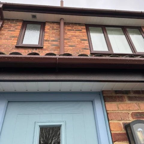 Image shows the front of a detached property in Wallisdown, Poole, with new Rosewood UPVC fascias, white UPVC tongue and groove soffits and brown square UPVC guttering and a bird guard system