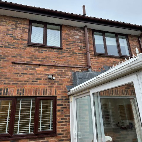 Image shows the back of a detached property in Wallisdown, Poole, with new Rosewood UPVC fascias, white UPVC tongue and groove soffits and brown square UPVC guttering over a conservatory