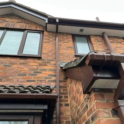 Image shows the front of a detached property in Wallisdown, Poole, with new Rosewood UPVC fascias and bargeboards, white UPVC tongue and groove soffits and brown square UPVC guttering