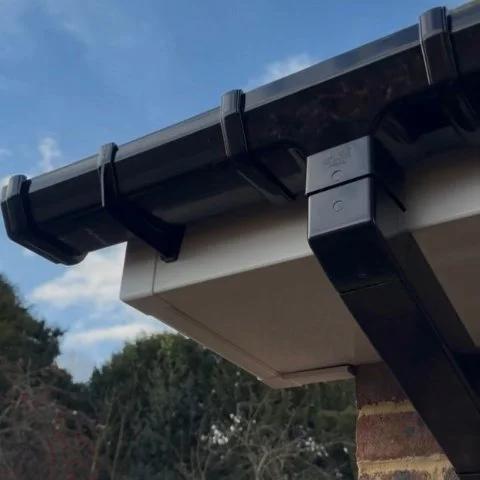 Image shows close up of replacement white UPVC fascias, white UPVC soffits and new black square UPVC guttering and downpipe in Wimborne Dorset
