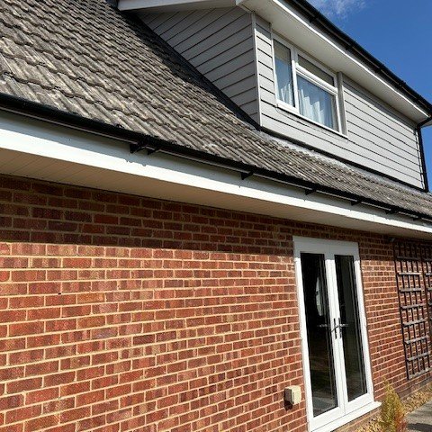 opposite side view of the side of the bungalow showing newly fitted white UPVC fascias and soffits with black round guttering