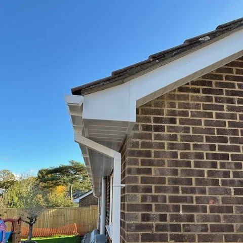 Close-up of the corner of a brick house showing new white bargeboards and a one piece box end in white upvc