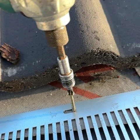 Image shows close up of drill as metal birdcomb bird guard system is being installed under tiles in Christchurch, Dorset