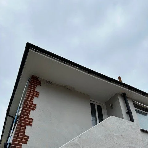 close up of white tongue and groove soffits with black guttering fitted over the porch of a maisonette