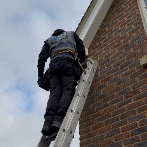 Image shows fitter on a ladder at detached property in Wimborne Dorset replacing white UPVC fascias, white UPVC soffits and white UPVC bargeboards and new black square UPVC guttering and downpipes
