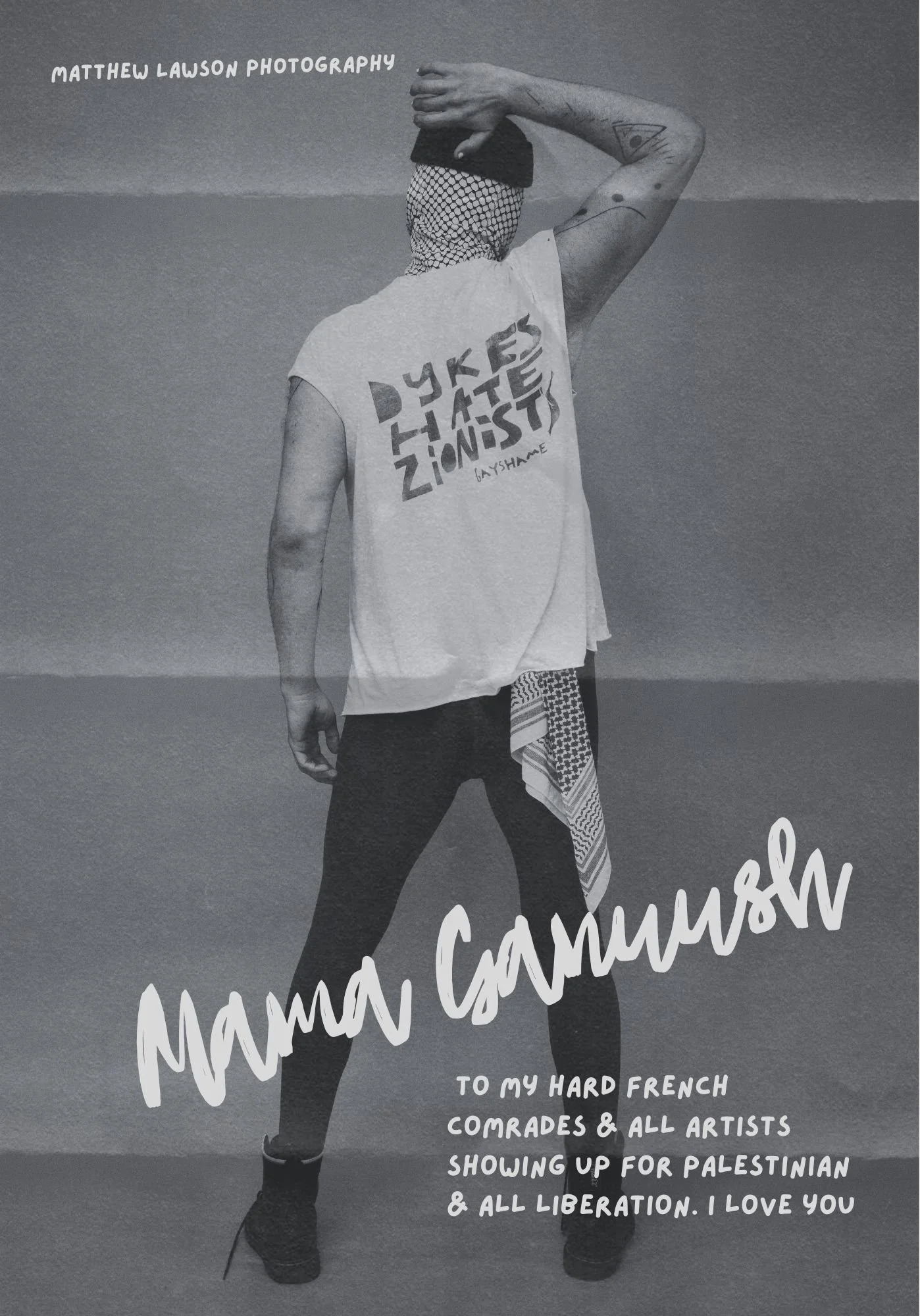 Black and white photo of a person standing on the beach holding a phone to take a selfie, wearing a bandana over their head, a sleeveless shirt with bold text, black pants, and high-heeled shoes. The shirt has the text 'Dykes Hate Zionists' and a sma