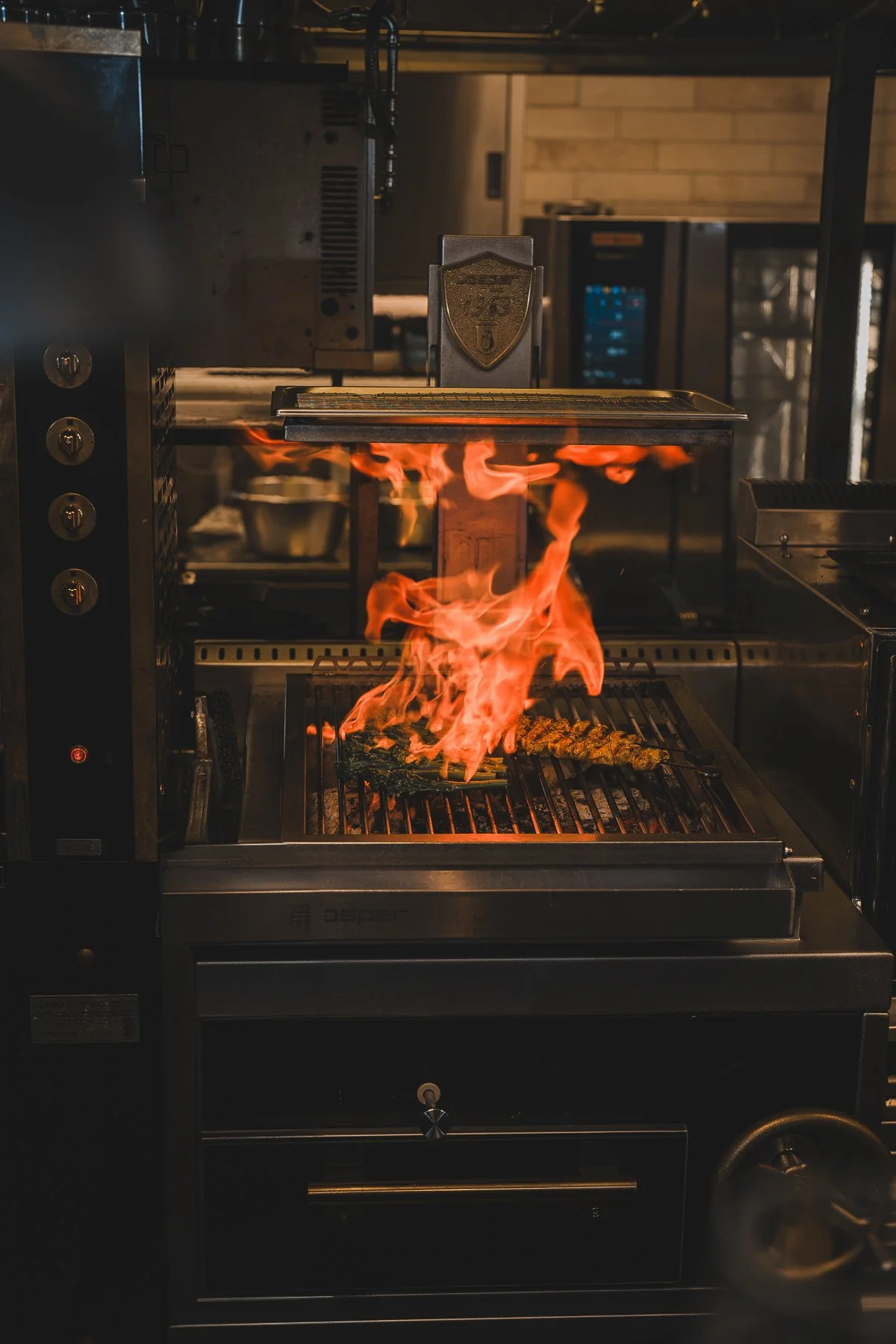 Flames rise as food is grilled on an open flame in a commercial kitchen.
