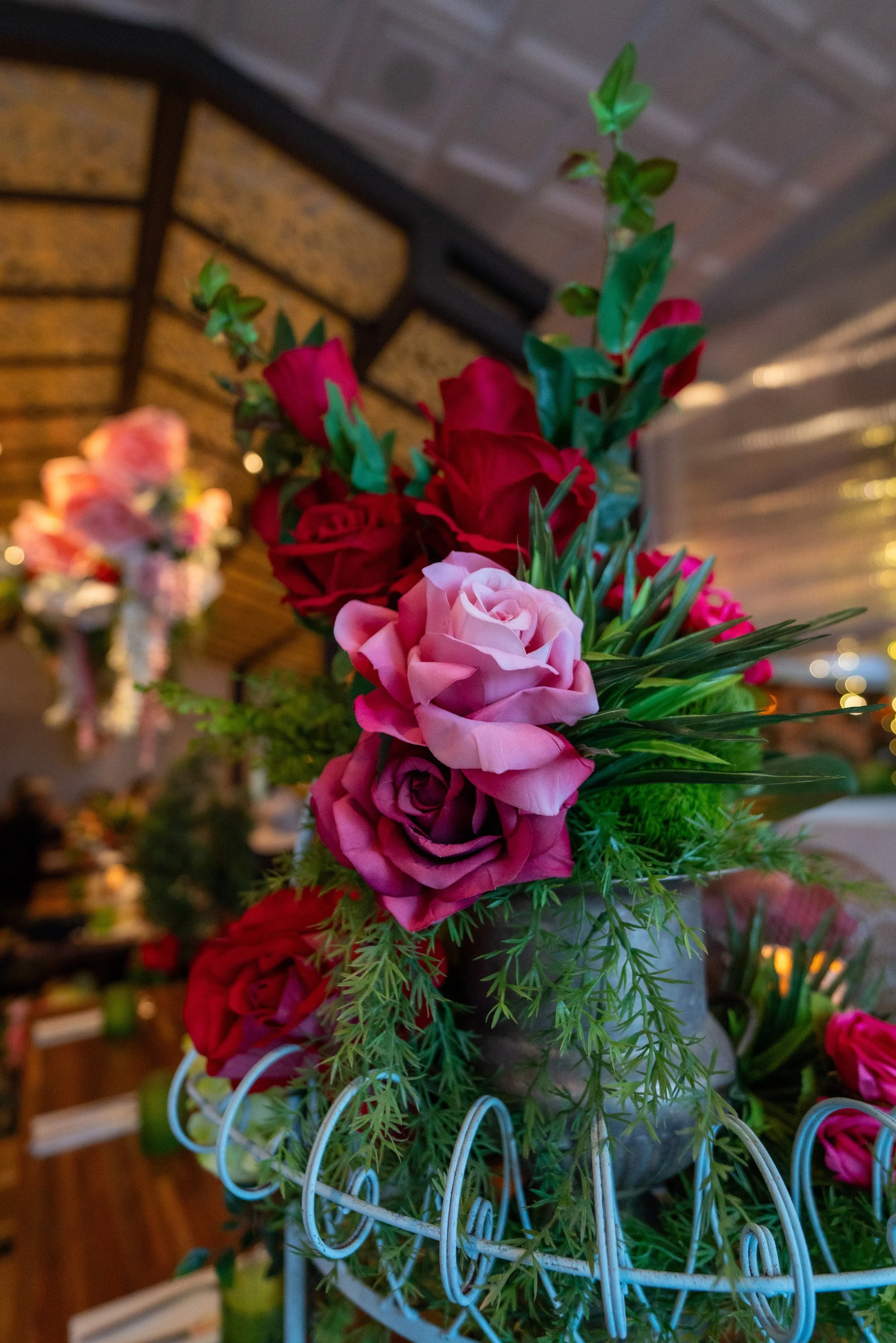 A colorful bouquet of pink and red roses with greenery in a vase, placed on a decorative stand.