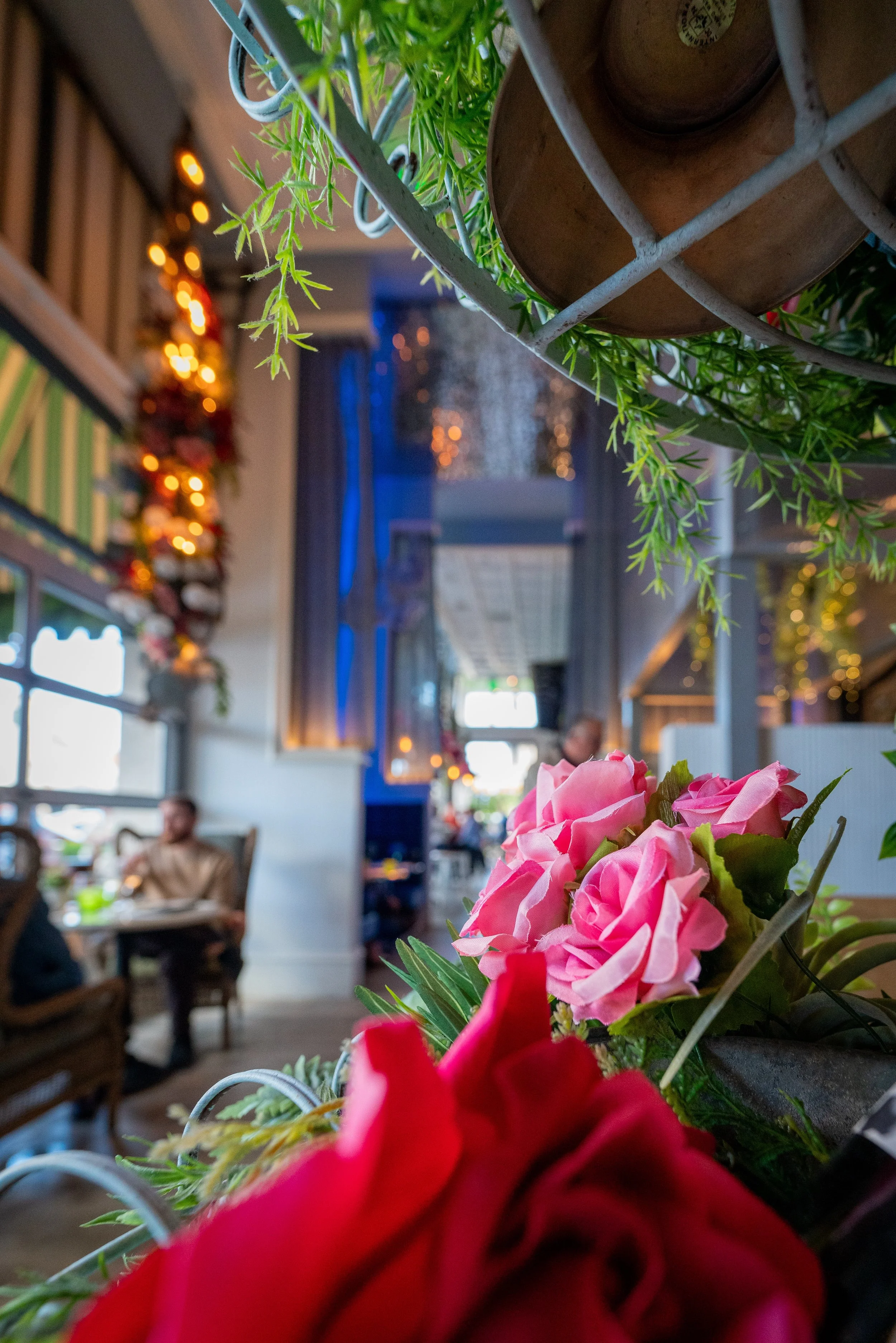 Close-up view of pink and red flowers on a table inside a decorated Queenstown Village restaurant with blurred diners, Christmas decorations, and cozy lighting.