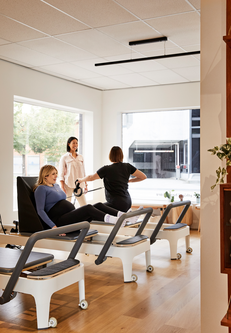 Pilates instructor teaching reformer pilates class with two pregnant women.