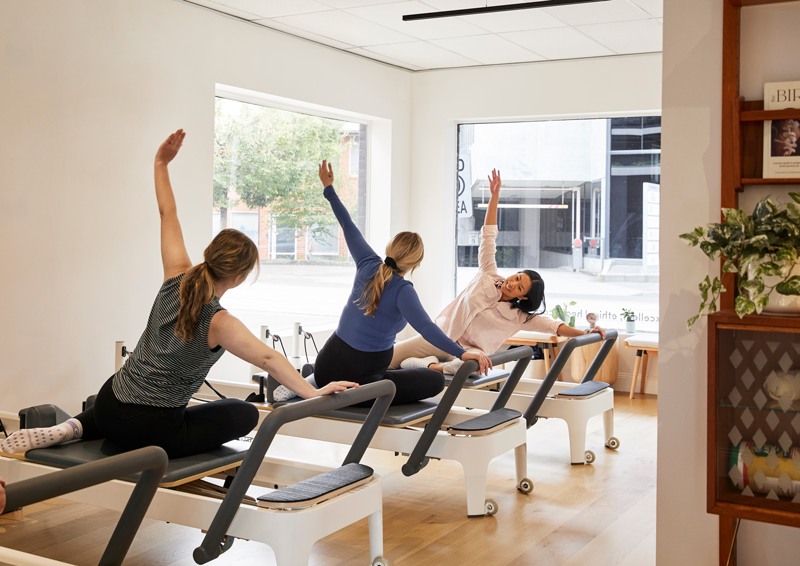 Woman Pilates instructor, teaching two pregnant women on reformers in pilates studio.