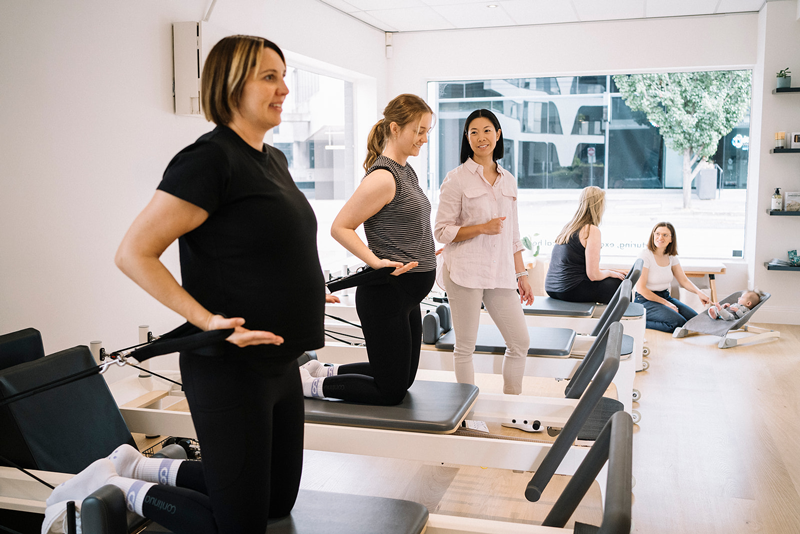 Pilates instructor guiding prenatal reformer pilates class in bright pilates studio.