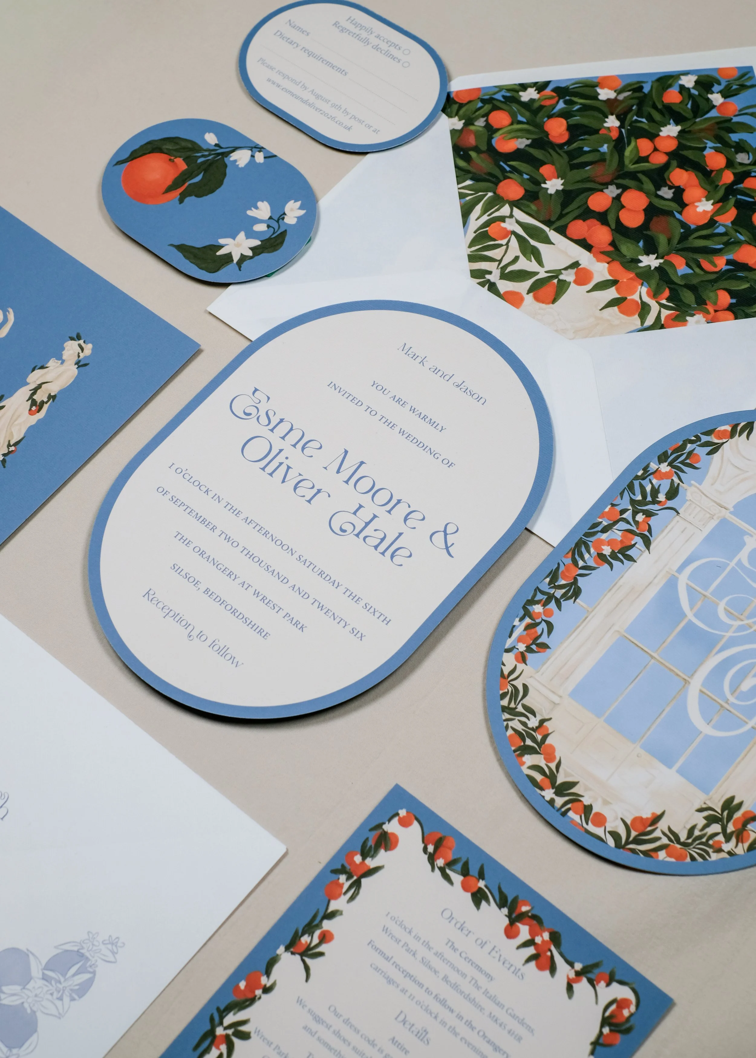 Flat lay of The Orangery wedding stationery suite on fine-line textured paper, featuring arch-shaped invitations with a sunlit glasshouse window illustration, citrus motifs, and an orange grove envelope liner.