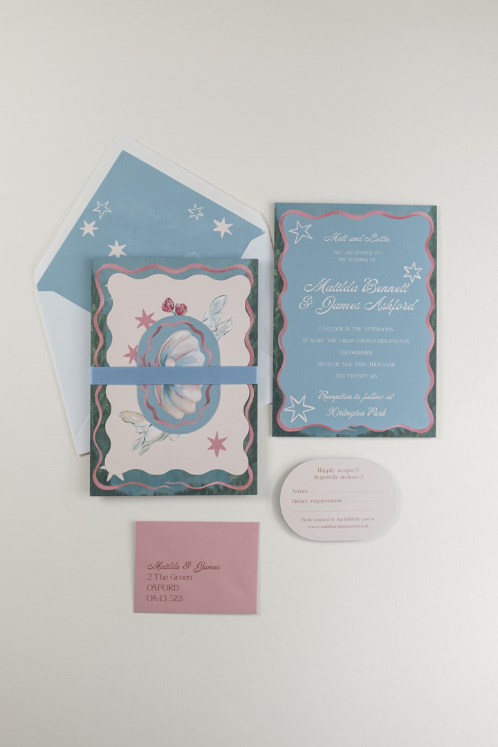 The Coquette wedding invitation suite bound by a cornflower blue double-faced satin ribbon band, displayed beside the flat-laid RSVP and invitation reverse details and envelope.