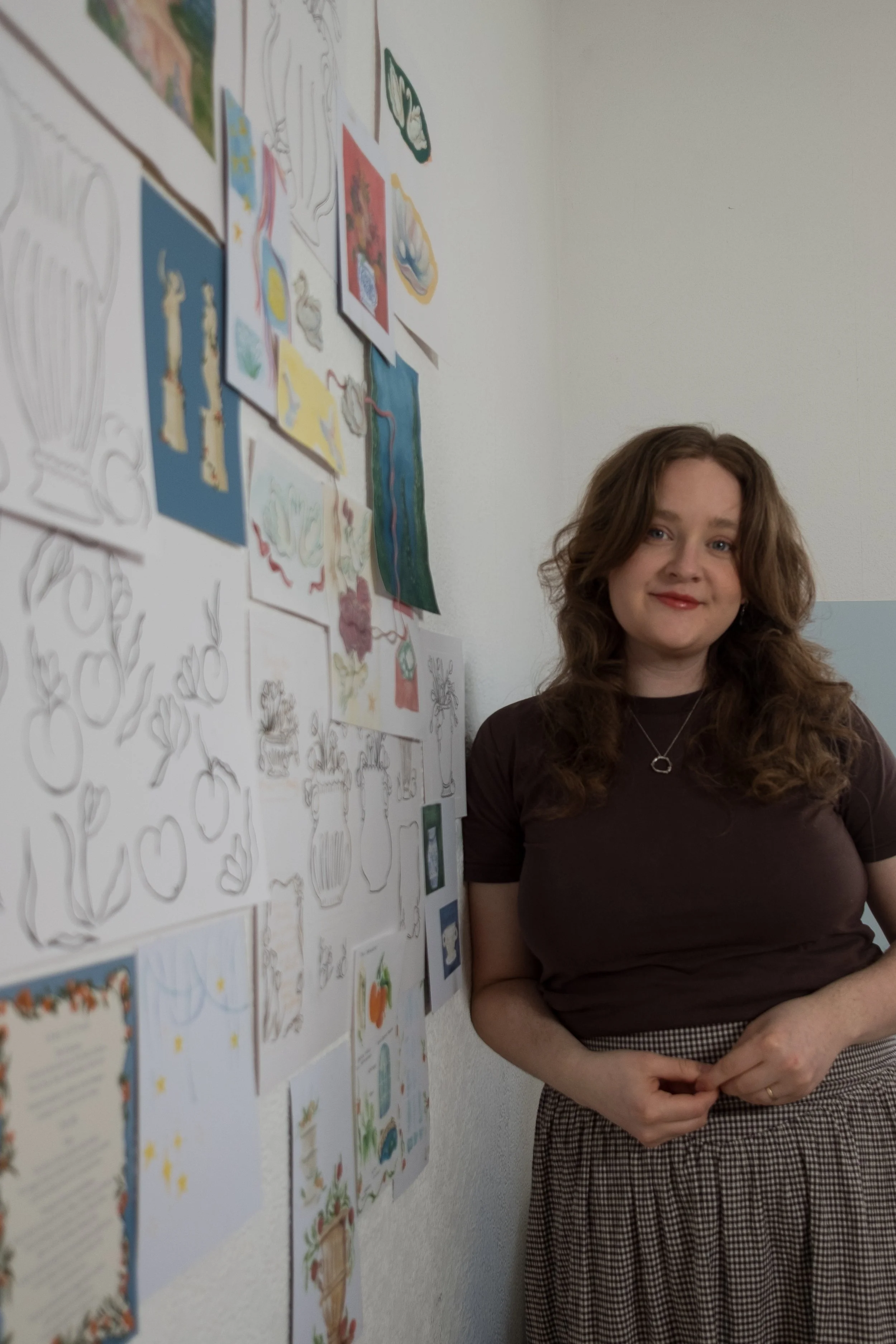 The artist and wedding stationery designer standing in her creative studio next to a wall of original sketches, gouache illustrations, and motifs.