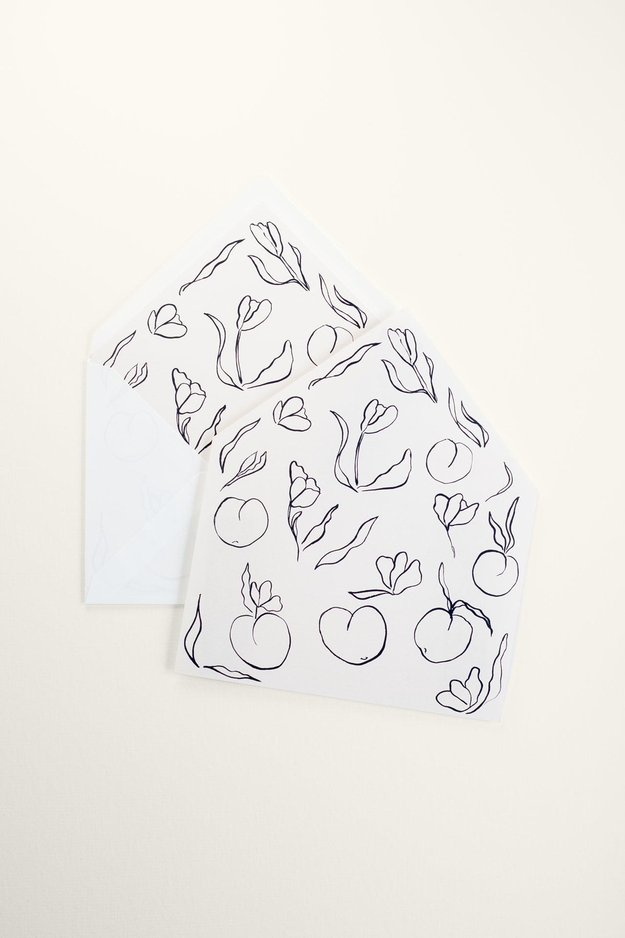 Flat Tulips wedding invitation envelope liner featuring an all-over print of black ink flowers and fruit, styled over an open envelope showing the inner lining.