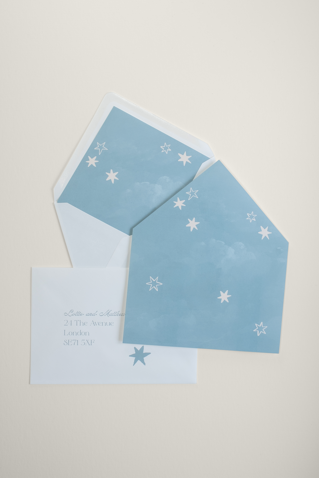 Flat lay of Coquette wedding envelopes and liners, displaying an envelope stuffed with the liner, the full painterly starry sky illustration, and an addressed envelope